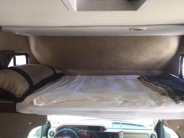 Cozy over-cab bunk bed in an RV rental, with white bedding, side windows, and ample space for sleeping.. Forest River Forester 2016