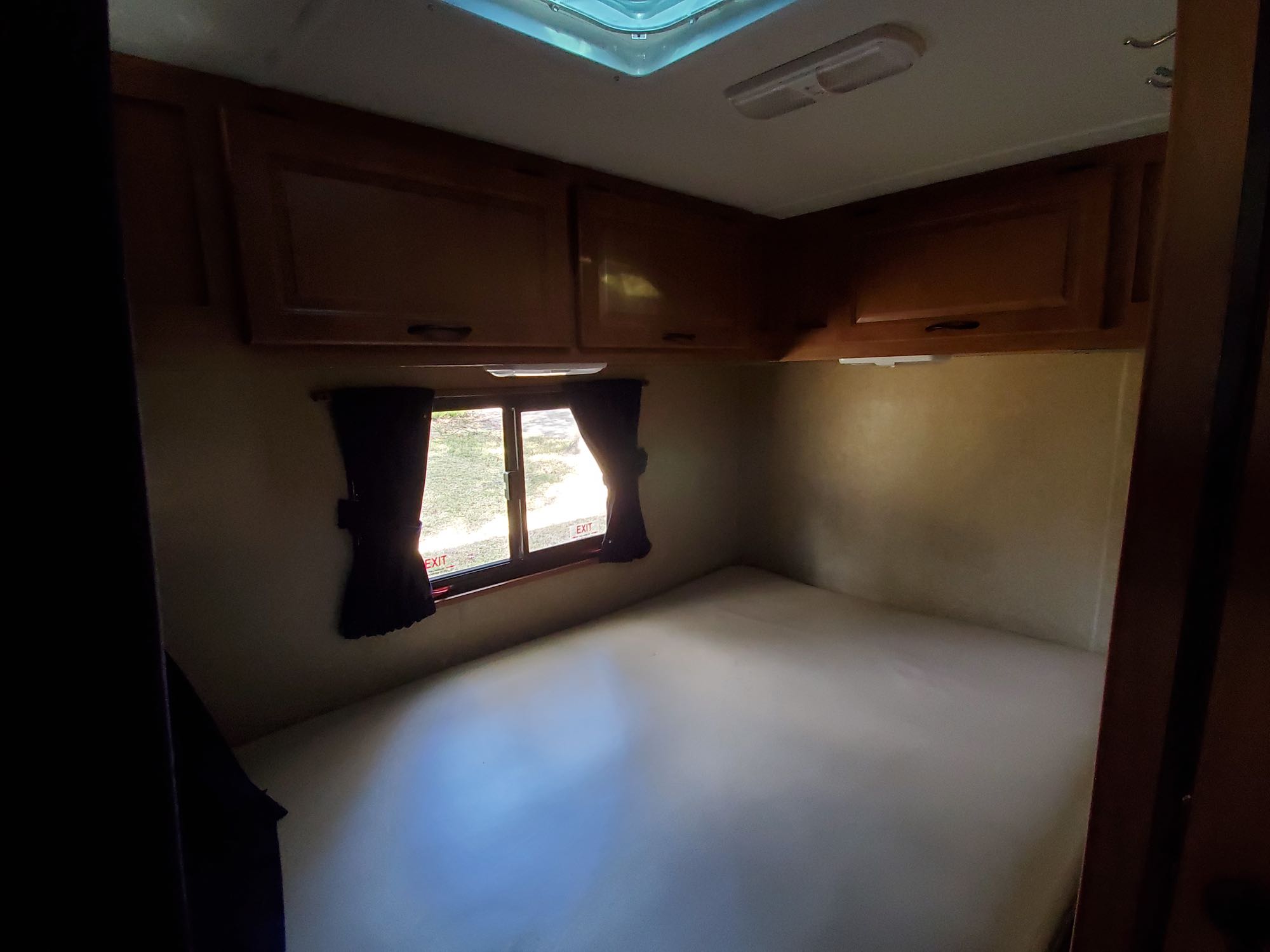 RV rental unfurnished bedroom interior with bed platform, overhead cabinets, and window.. Thor Motor Coach Four Winds Majestic 2016