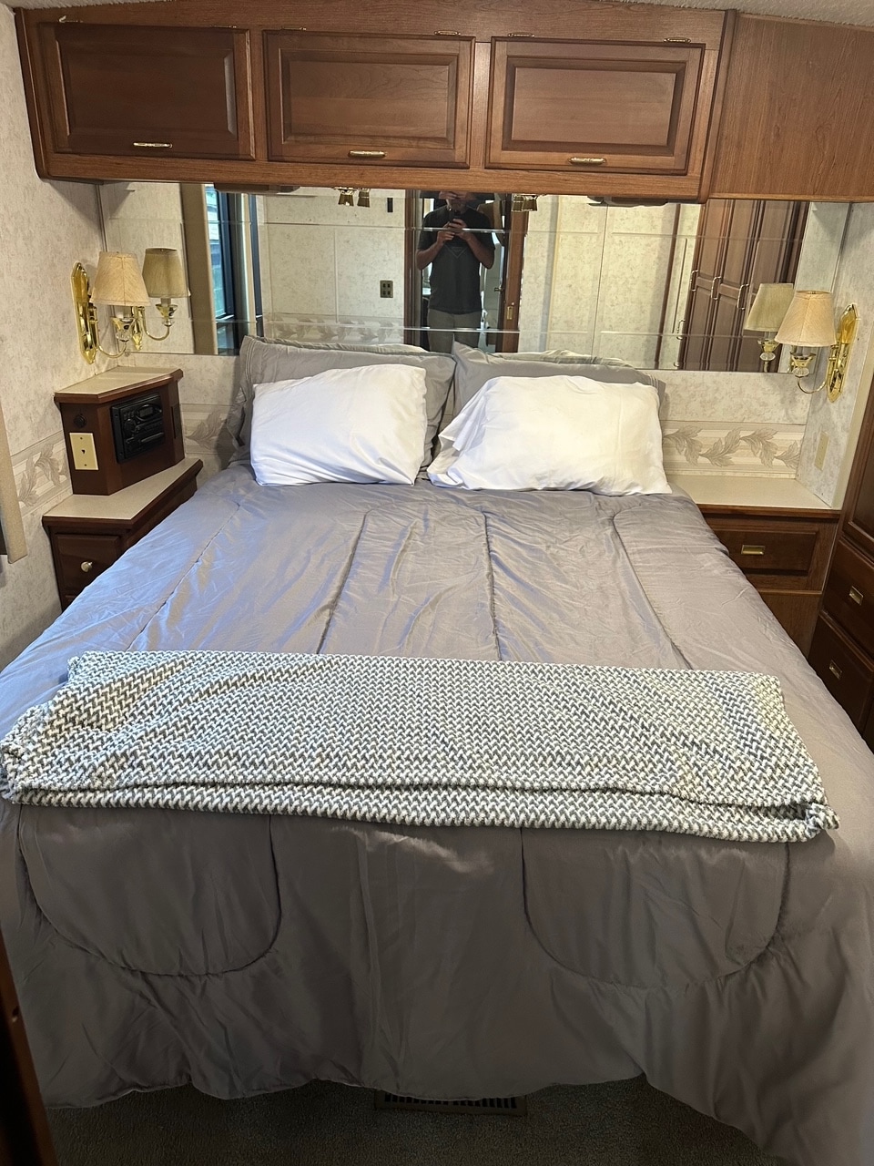 This RV rental bedroom features a comfy bed with gray linens, mirrored headboard, and wood cabinets above.. Winnebago Journey DL 2001