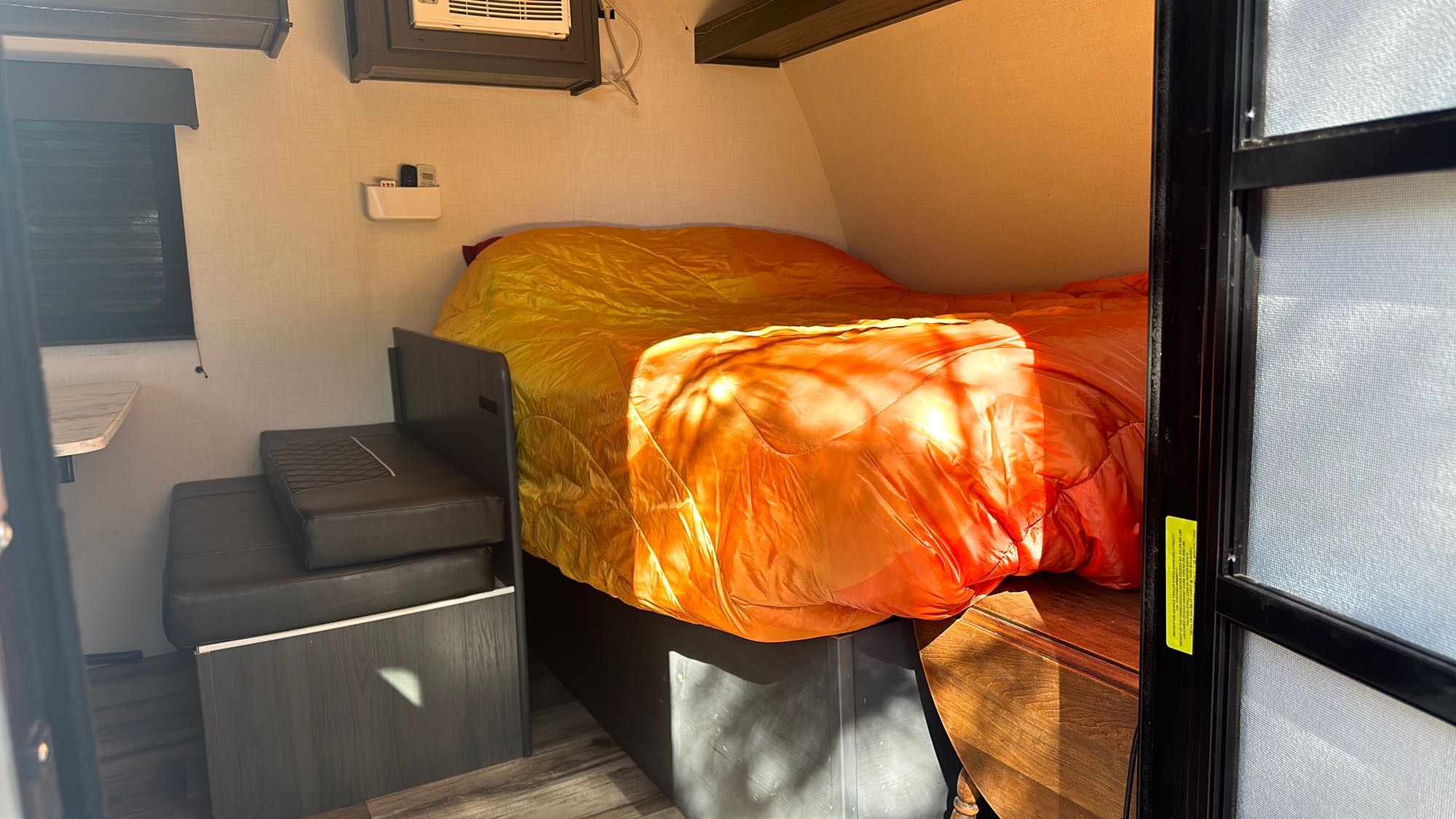 Inside an RV rental: a bright orange and yellow bed fills the right, with a compact dinette and AC unit to the left, ready for travel.. Dutchmen Colorado 2024