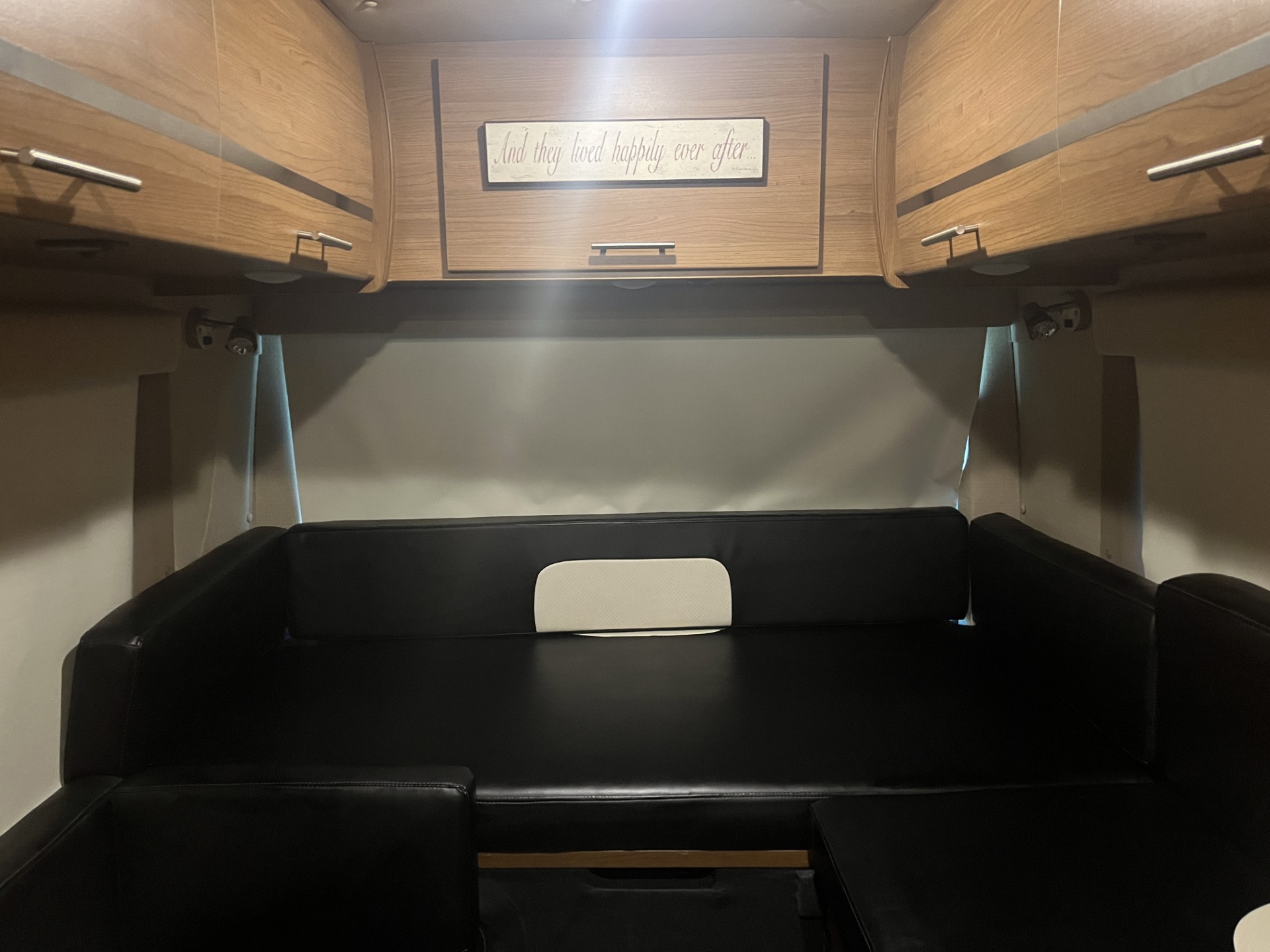 Cozy RV rental interior: black convertible seating/bed, overhead wood cabinets, and 'happily ever after' sign.. ERA ERA Class B 2014