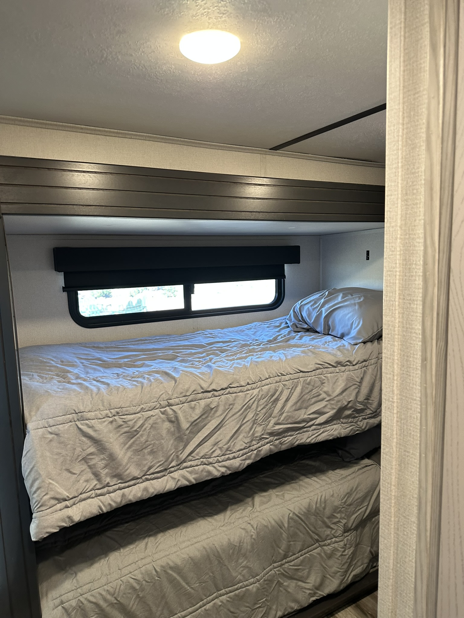 Inside an RV rental: a compact sleeping area with modern bunk beds. Features grey bedding and a window.. Keystone RV Montana High Country 2023