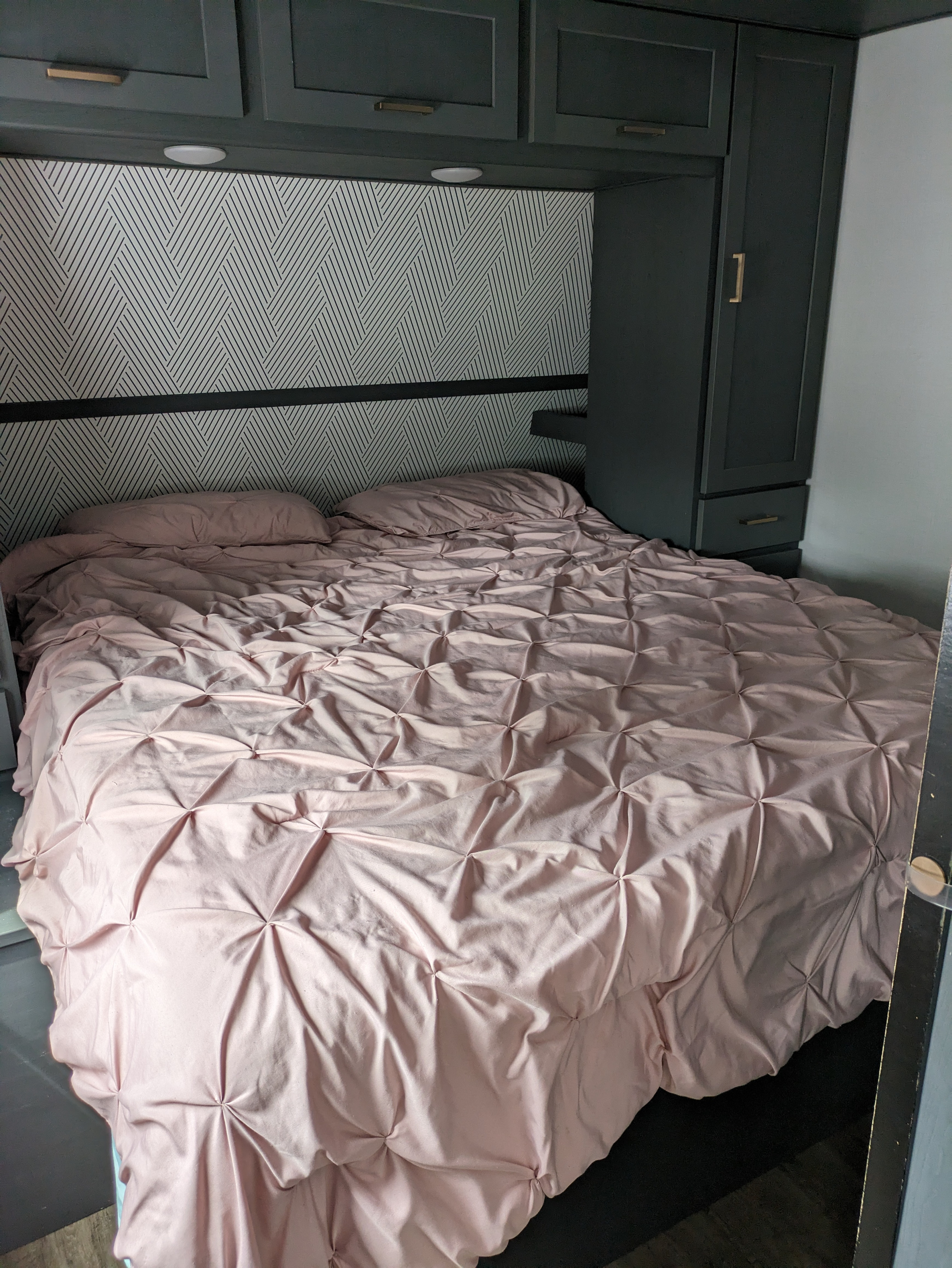 Stylish RV rental bedroom with a comfy pink comforter, geometric wallpaper, and dark grey storage cabinets.. Keystone RV Bullet Premier Ultra Lite 2022
