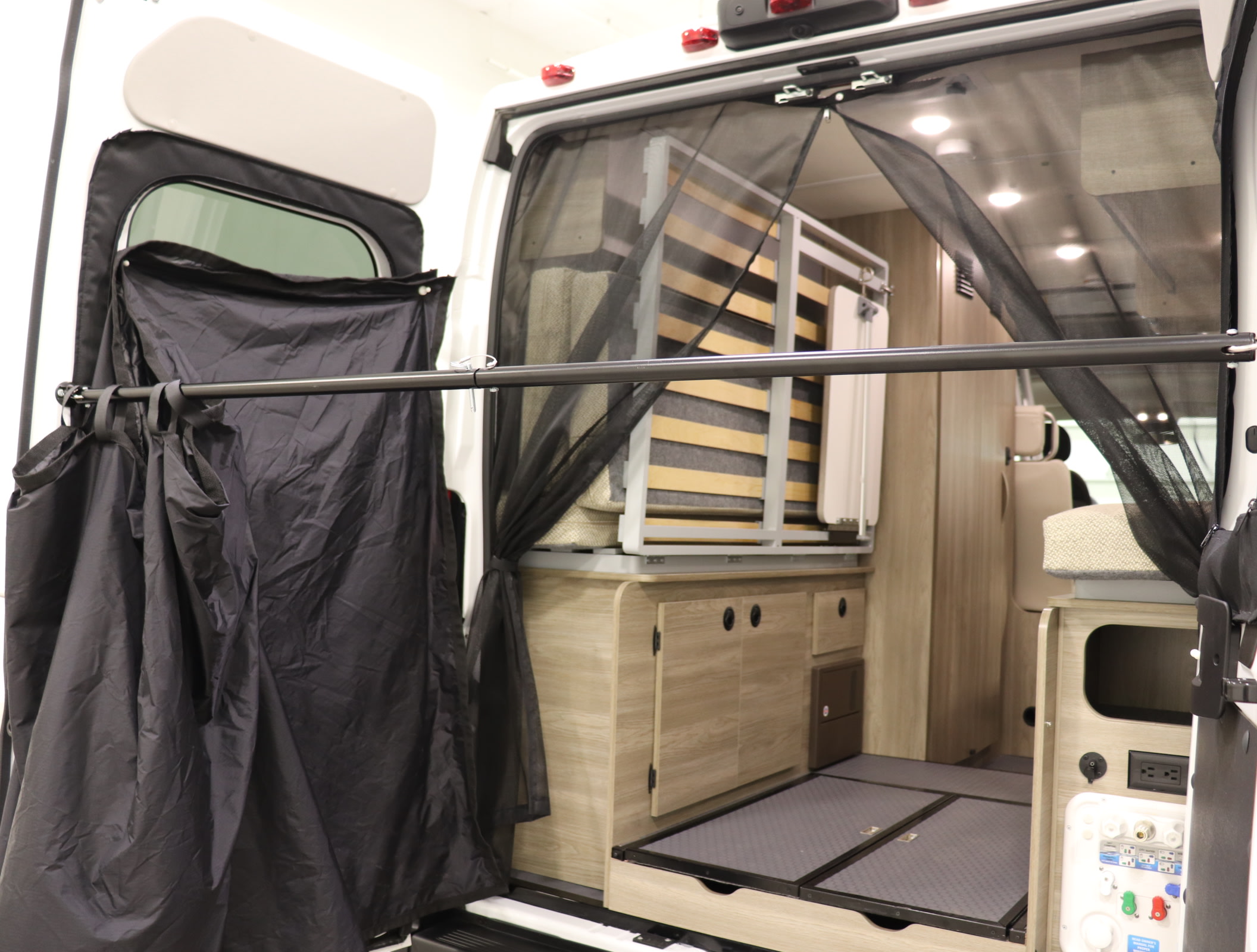 RV rental interior shows a modular bed/storage, black mesh screen, and a privacy curtain at the rear of the van.. Winnebago Solis 36A 2023