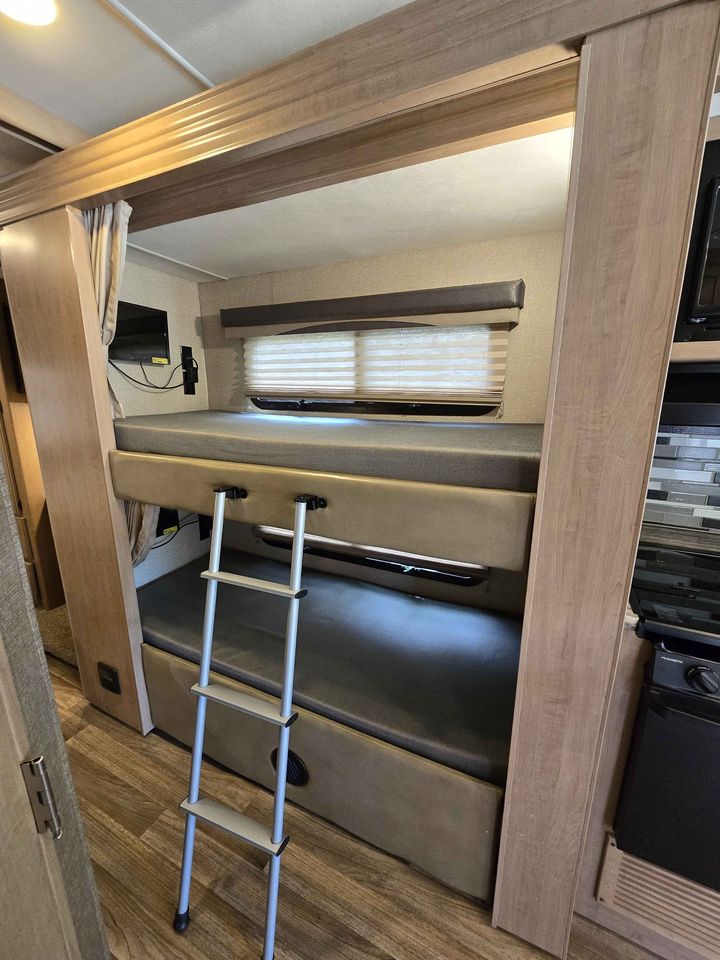 RV rental interior showing comfortable bunk beds with a ladder, window, and small TV, great for family travel.. Thor A.C.E. 2018