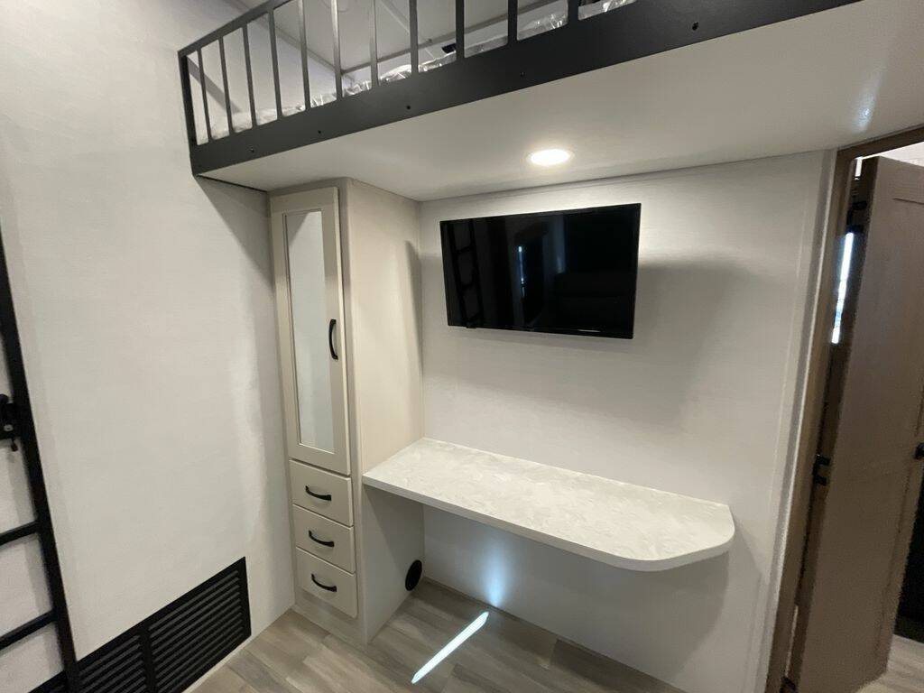 RV rental interior: loft bed, desk, wall-mounted TV, & built-in storage cabinet.. Alliance RV Paradigm 2024