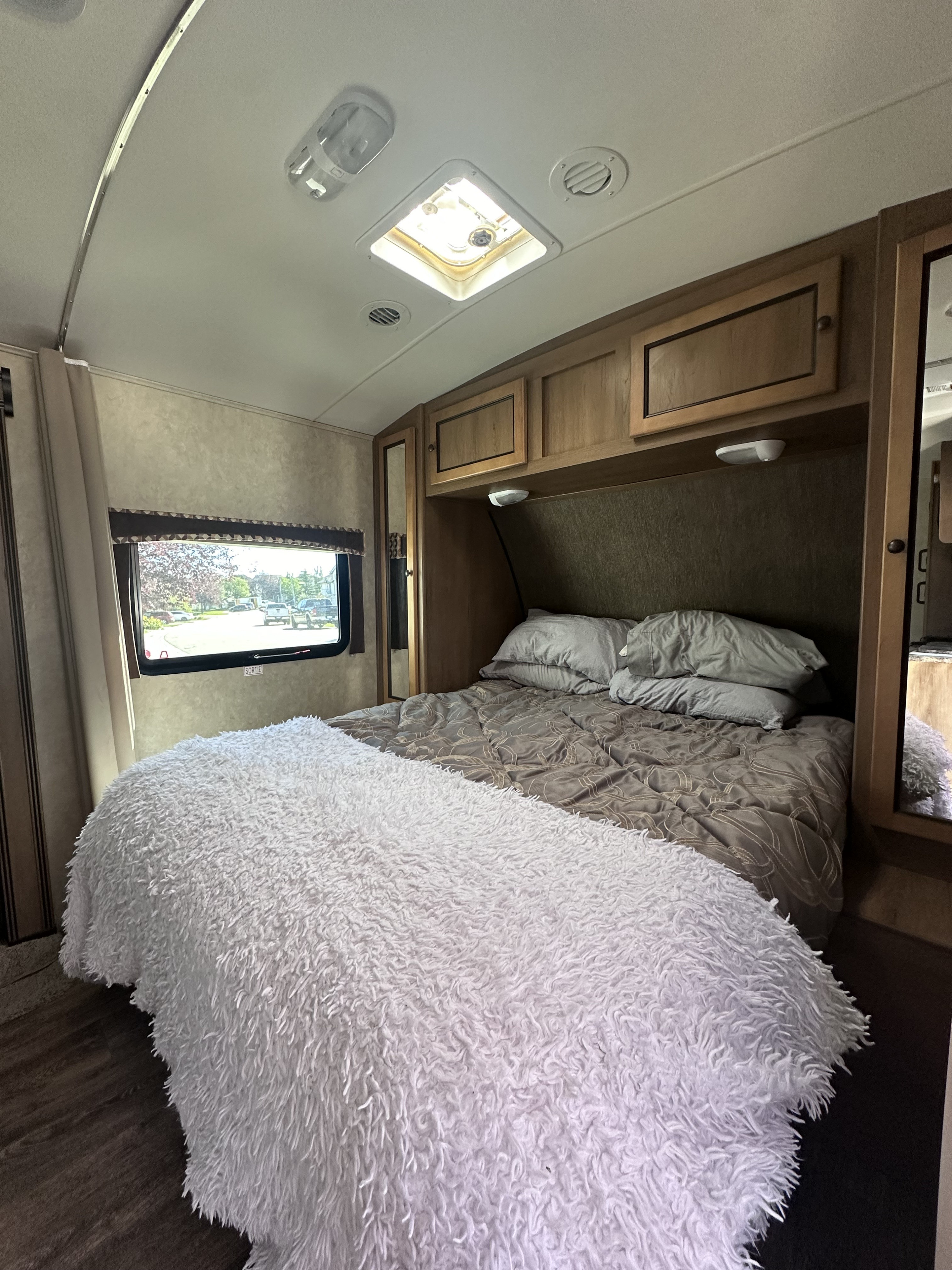Inside a cozy RV rental bedroom: bed with white fluffy blanket, cabinets, window, and ceiling vents.. Cruiser RV Shadow Cruiser 2016