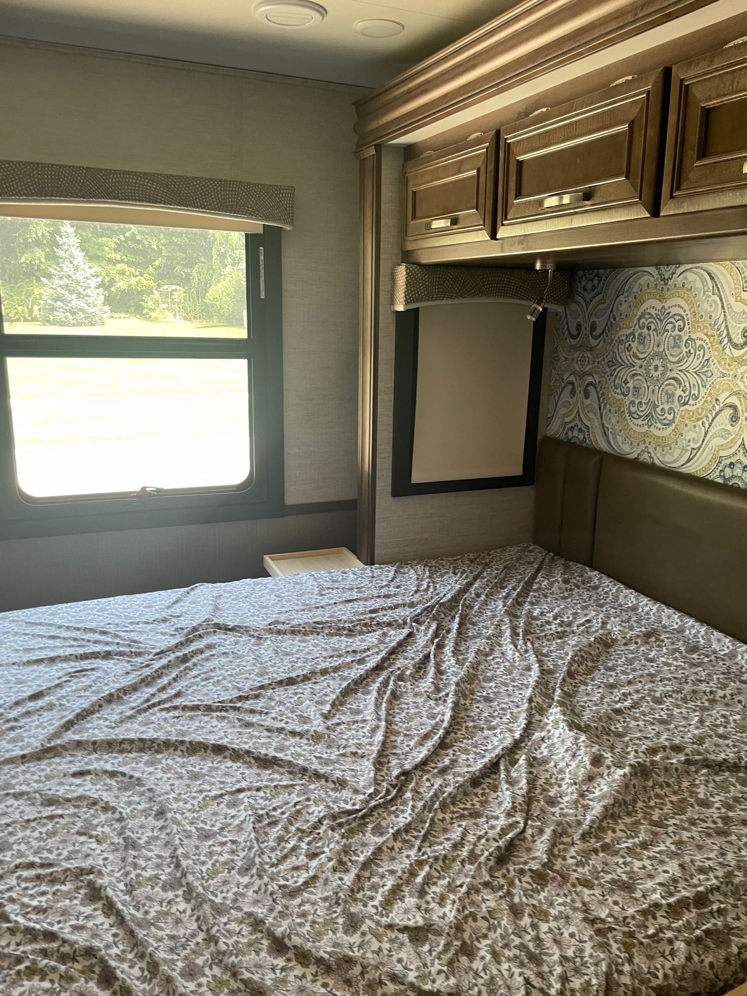 RV rental bedroom with patterned sheets, window view, and overhead storage cabinets.. Entegra Coach Vision 2021