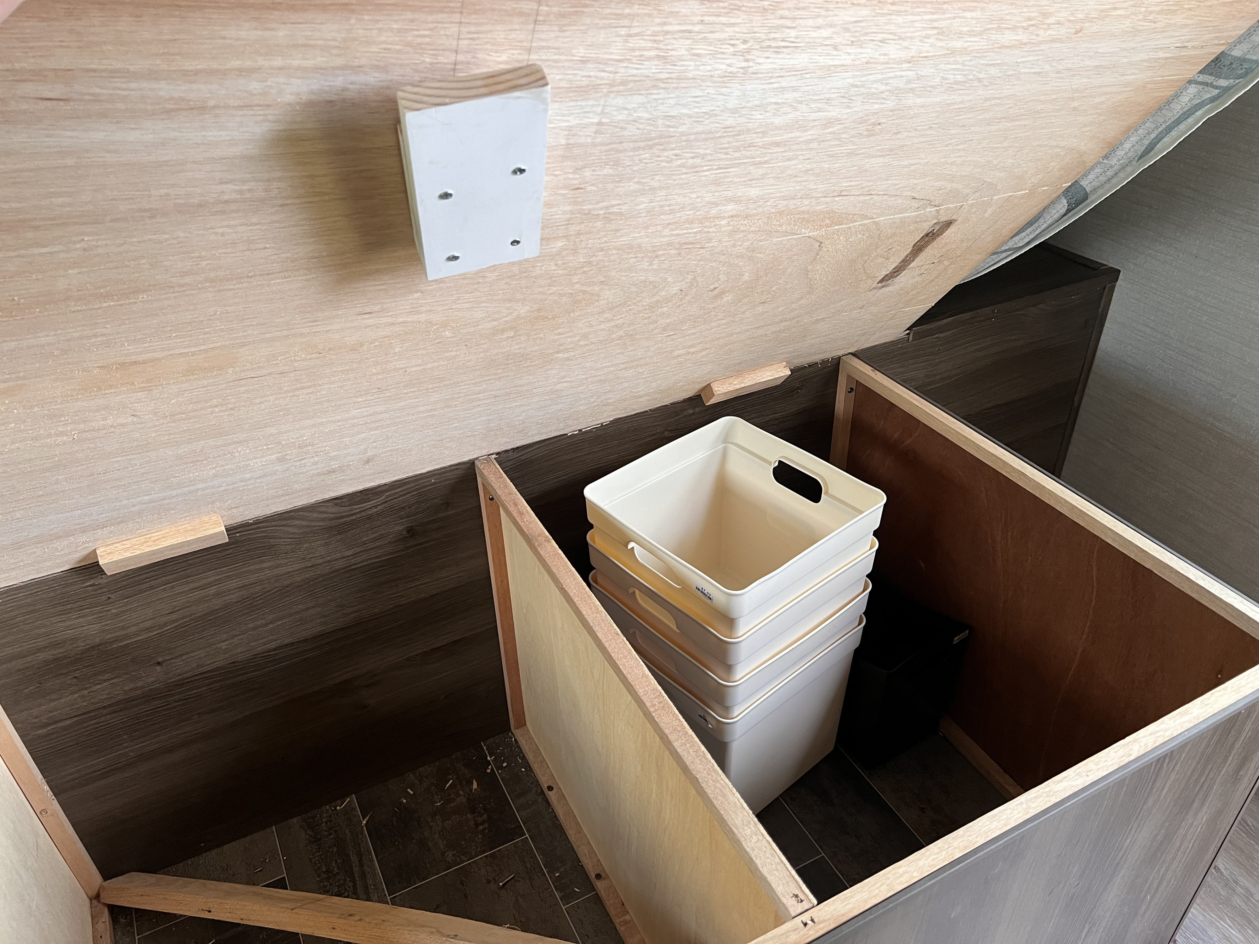 Open RV rental bed storage: wooden interior with support blocks & stacked white bins. Efficient space for your travel gear.. Keystone RV Bullet Ultra Lite 2019