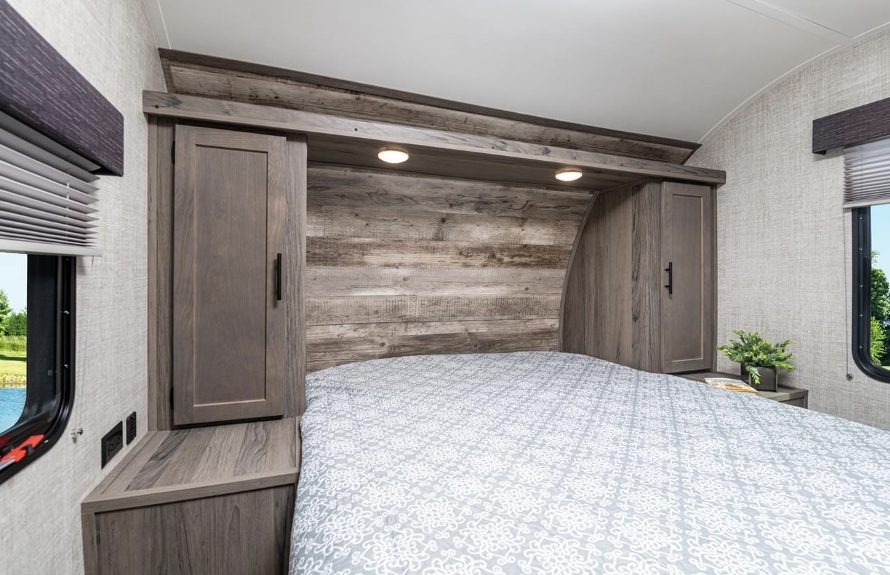 Comfortable RV rental bedroom with a stylish wood headboard, integrated lighting, storage, and scenic window views.. Gulf Stream Ameri-Lite 2024