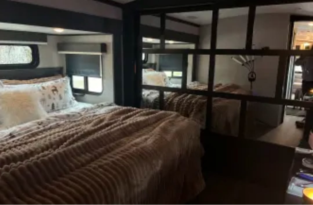 Explore this cozy RV rental bedroom with a plush bed, patterned bedding, and scenic windows, perfect for comfortable travel.. Jayco North Point 2023