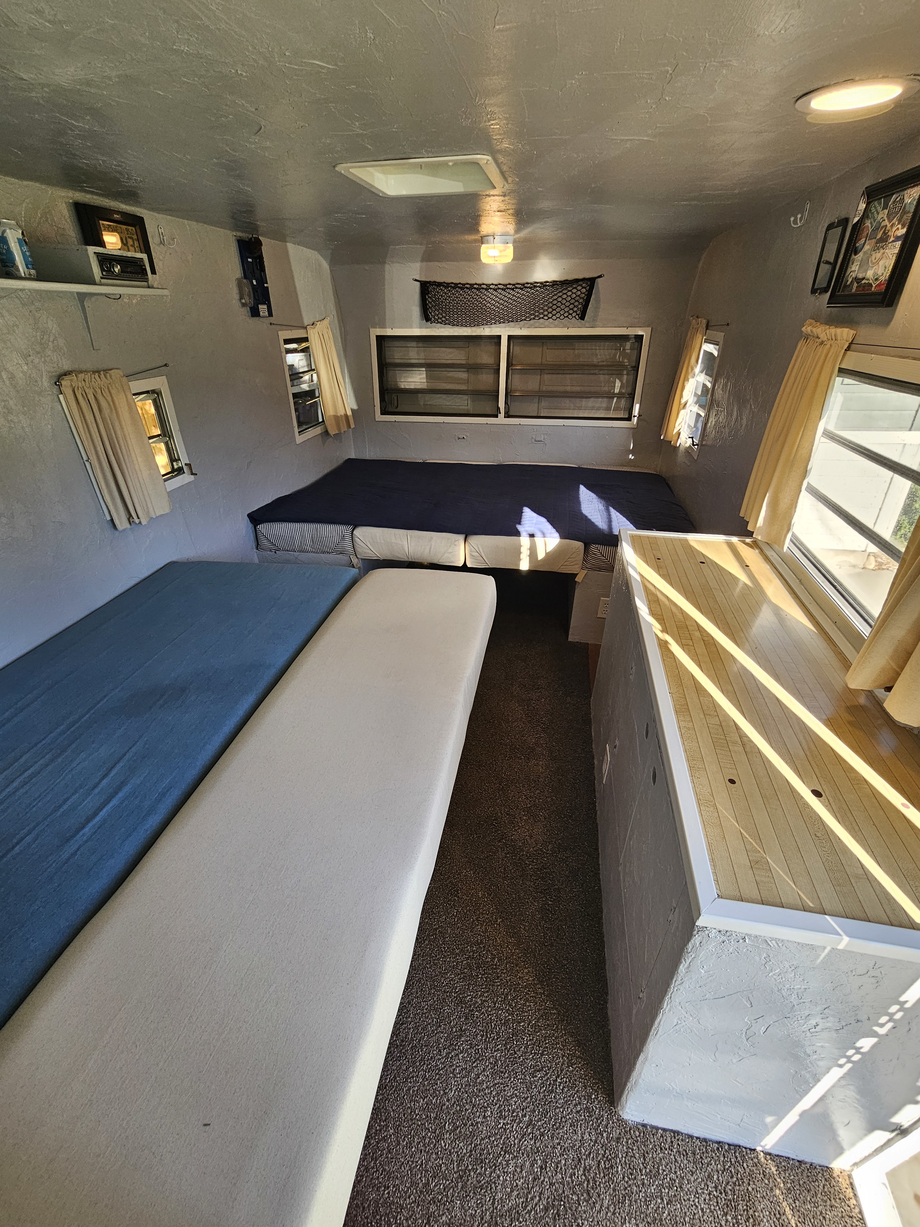 Bright RV rental interior: blue and beige beds, gray textured walls, carpeted floor, and sunlit wood counter.. Yellowstone B21539 - 19' 1967