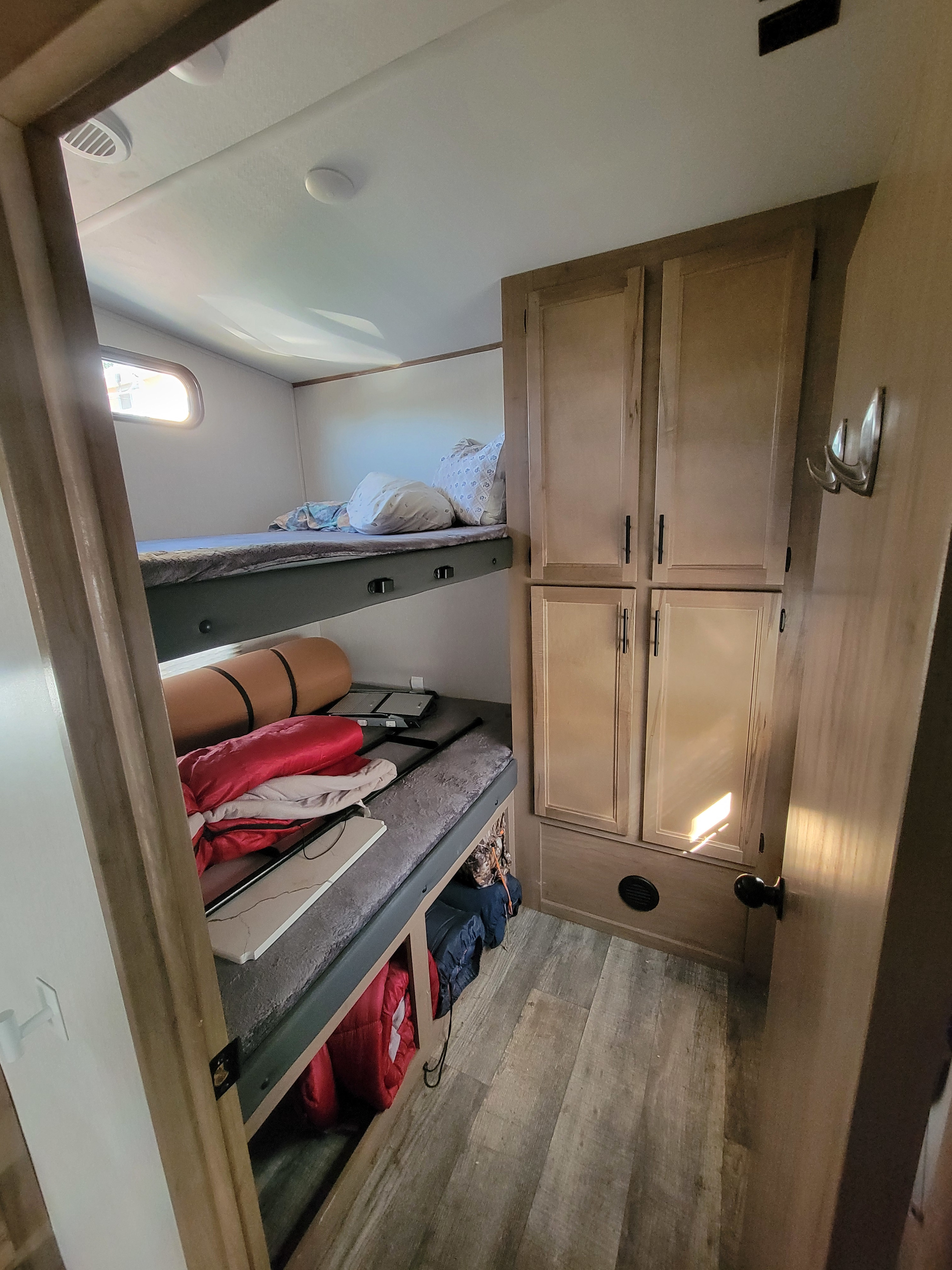 RV rental interior: cozy bunk beds with bedding, storage cabinets, and wood-look flooring for comfortable travel.. Forest River Cherokee Arctic Wolf 2023