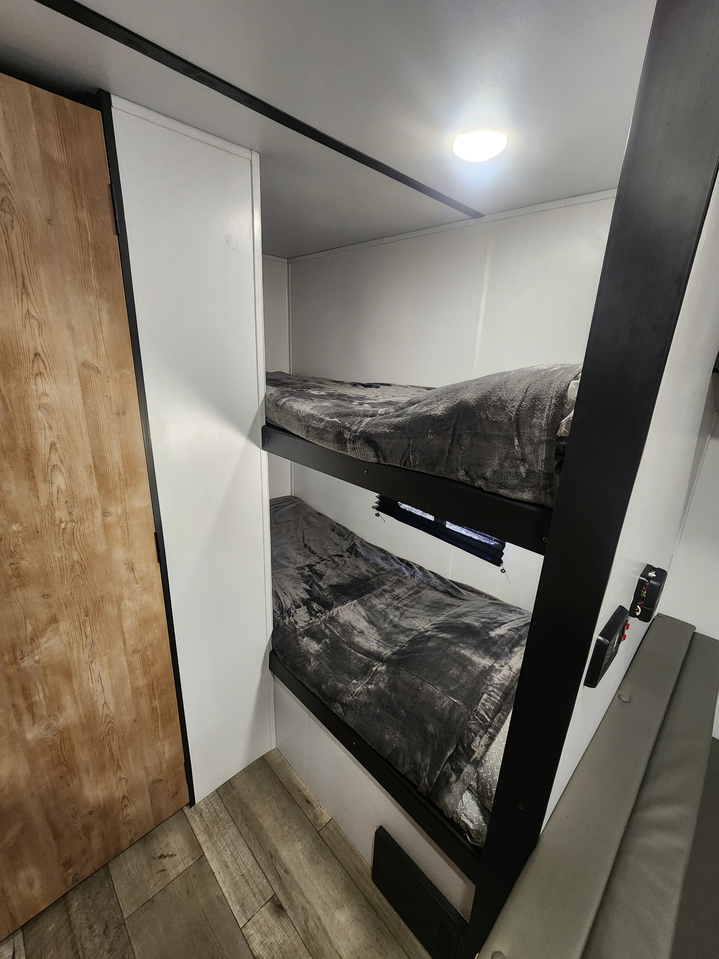 Inside an RV rental, showing compact bunk beds with cozy gray blankets and a light wood floor.. Keystone RV Springdale 2022