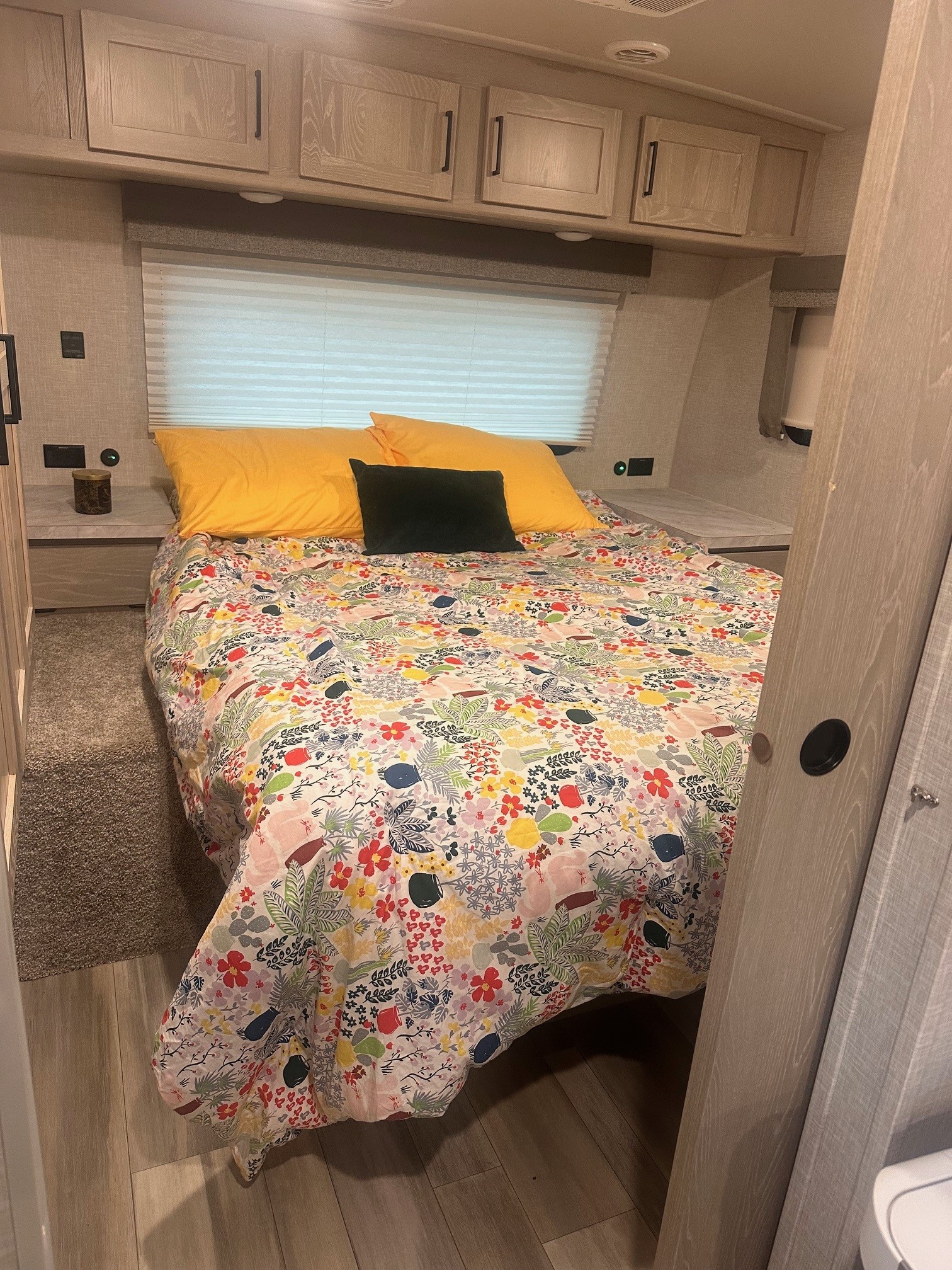 Cozy RV rental bedroom with floral bedding, yellow pillows, overhead cabinets, & a window.. Forest River Flagstaff Super Lite 2023