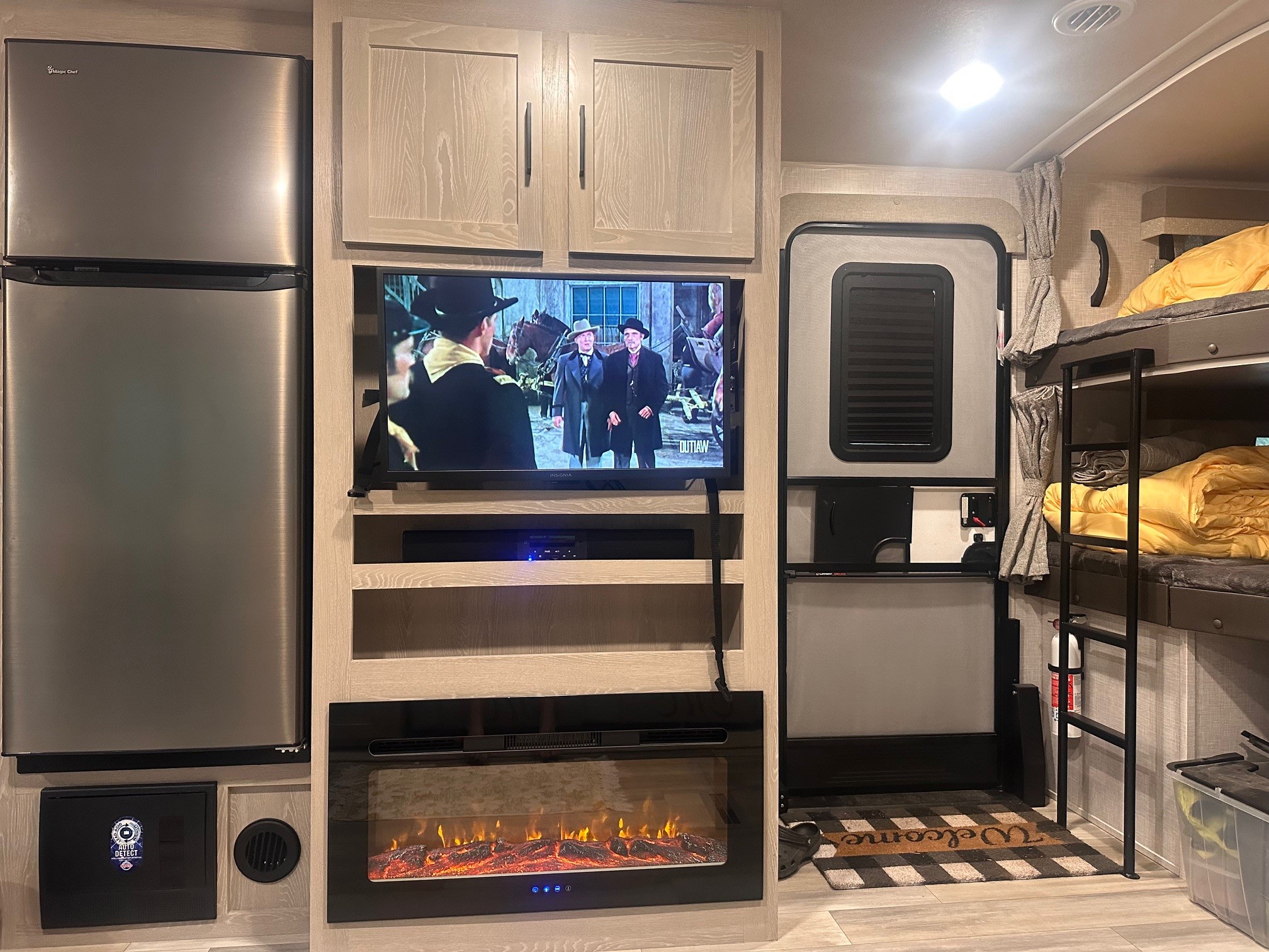 RV rental interior showing a fridge, TV, fireplace, bunk beds with yellow covers, and a welcome mat at the door.. Forest River Flagstaff Super Lite 2023