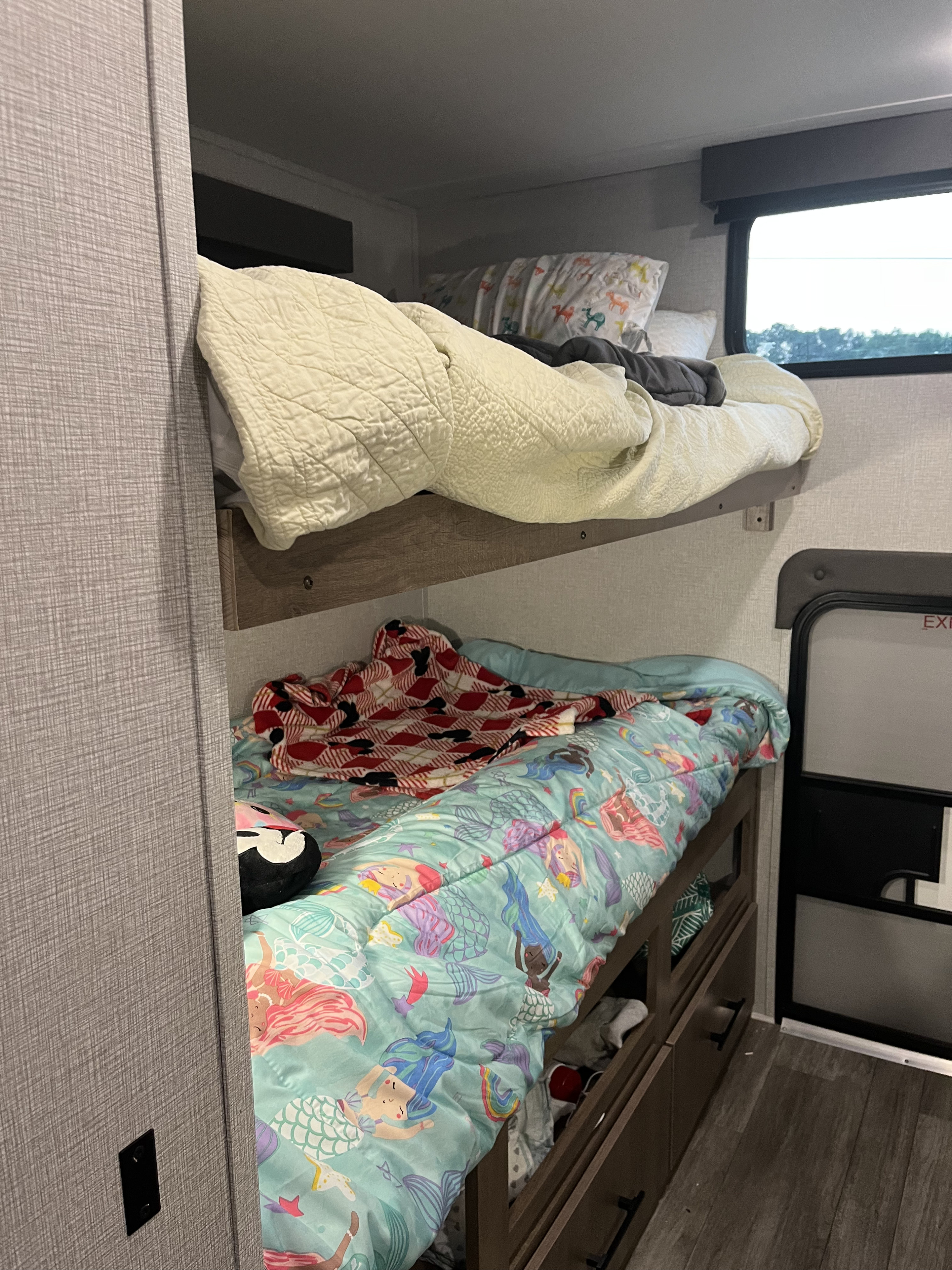 Interior of an RV rental, showcasing bunk beds with mermaid and animal-themed bedding, plus practical under-bed storage drawers.. Grand Design Imagine XLS 2023