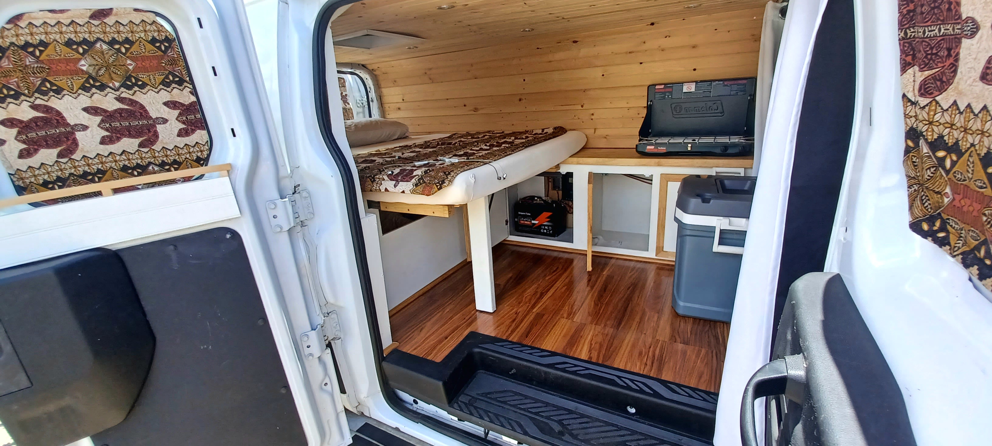 Cozy RV rental interior: wood-paneled camper van with a bed, stove, and cooler, seen through open side door.. Other Ford Transit 250 2015