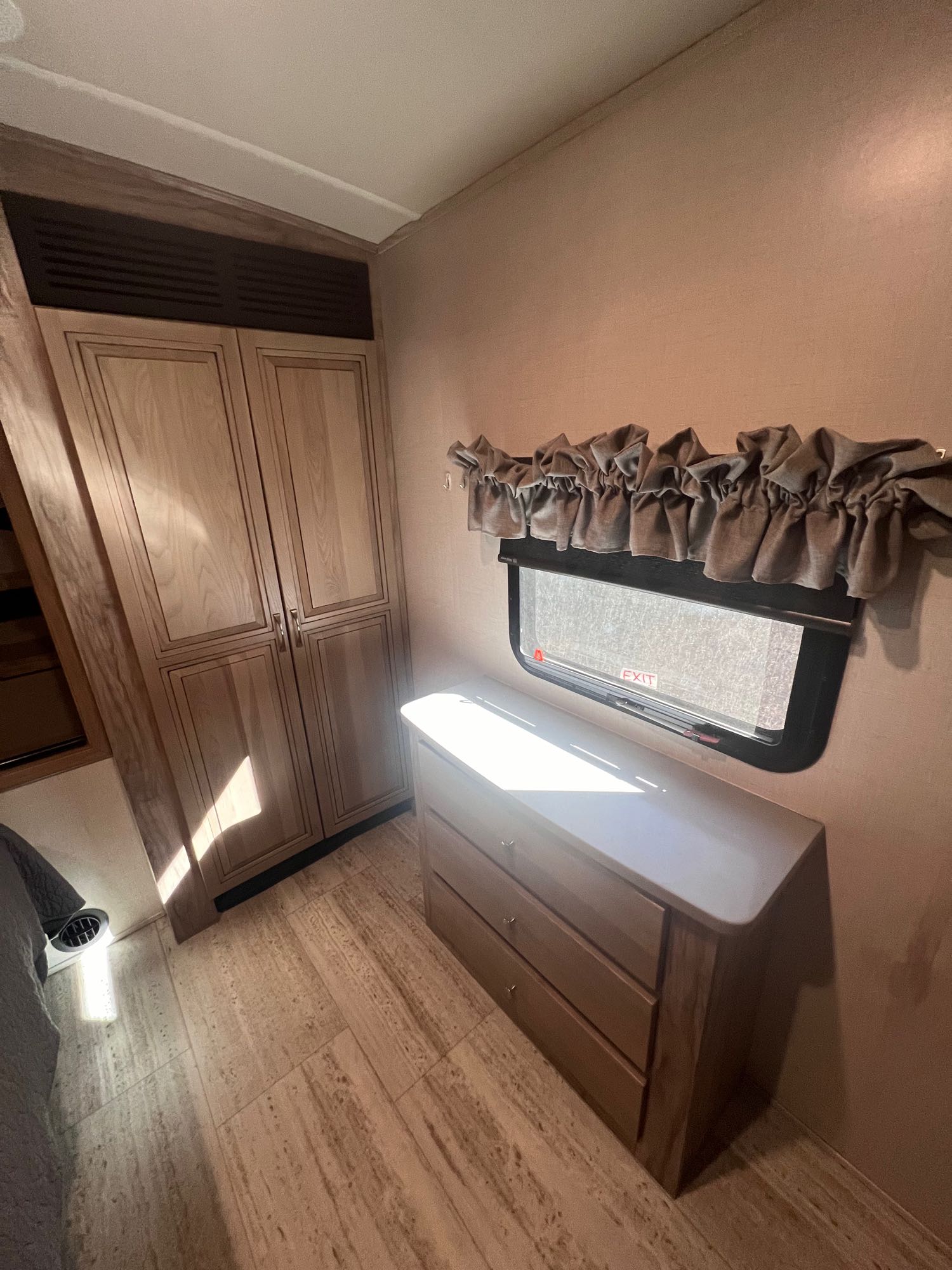 Spacious RV rental bedroom featuring a light wood closet, dresser, and a window with valance for ample storage.. Forest River Palomino Solaire 2021