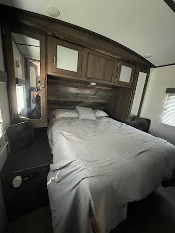 Spacious RV rental bedroom featuring a comfortable bed, wood-paneled walls, overhead cabinets, and a mirrored closet.. Keystone RV Passport Grand Touring 2019