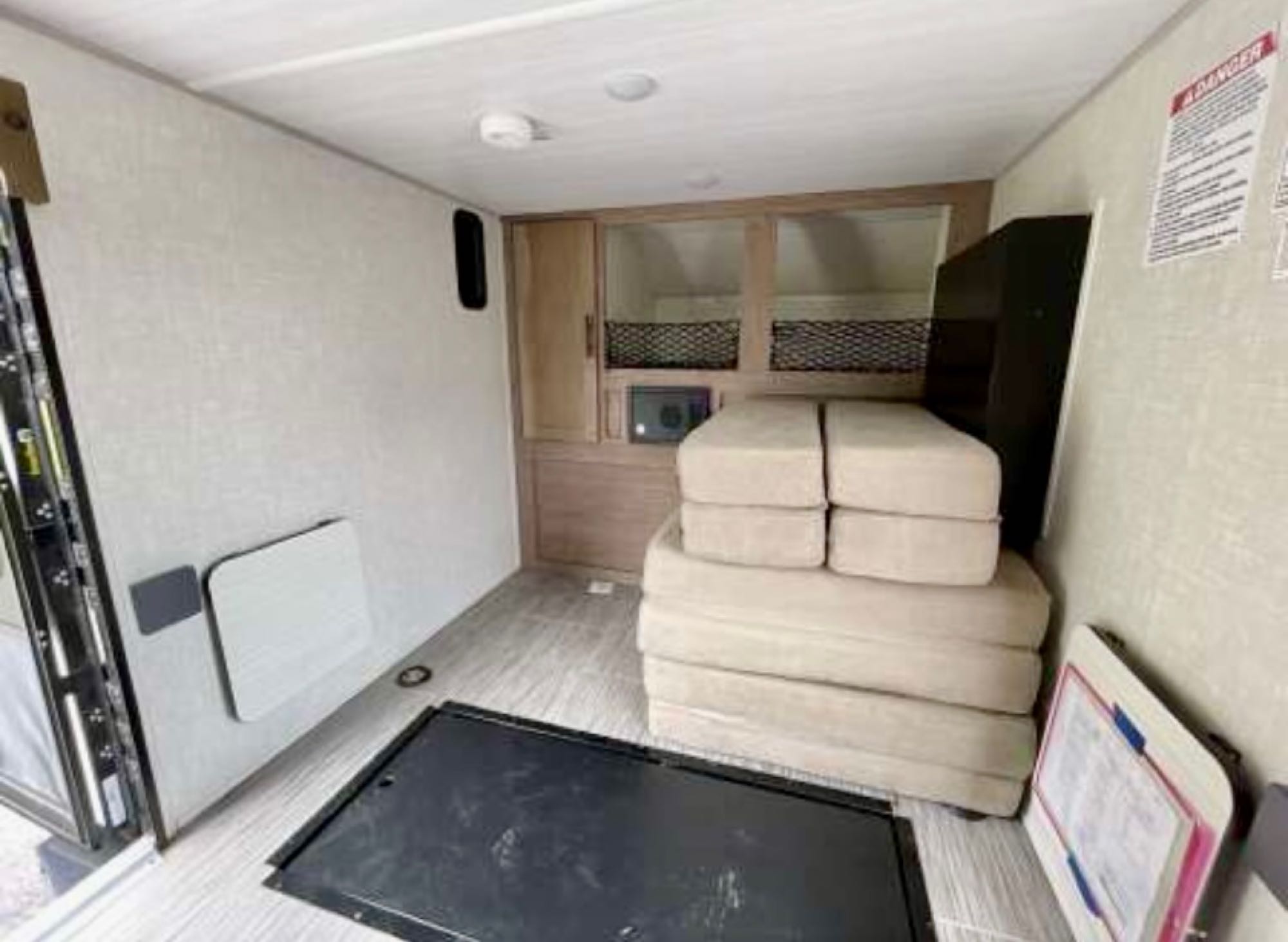Inside an RV rental: a flexible living space with light walls, wood cabinets, stacked cushions, and open side door.. Forest River NoBo 10.6 off grid mini toy hauler 2020