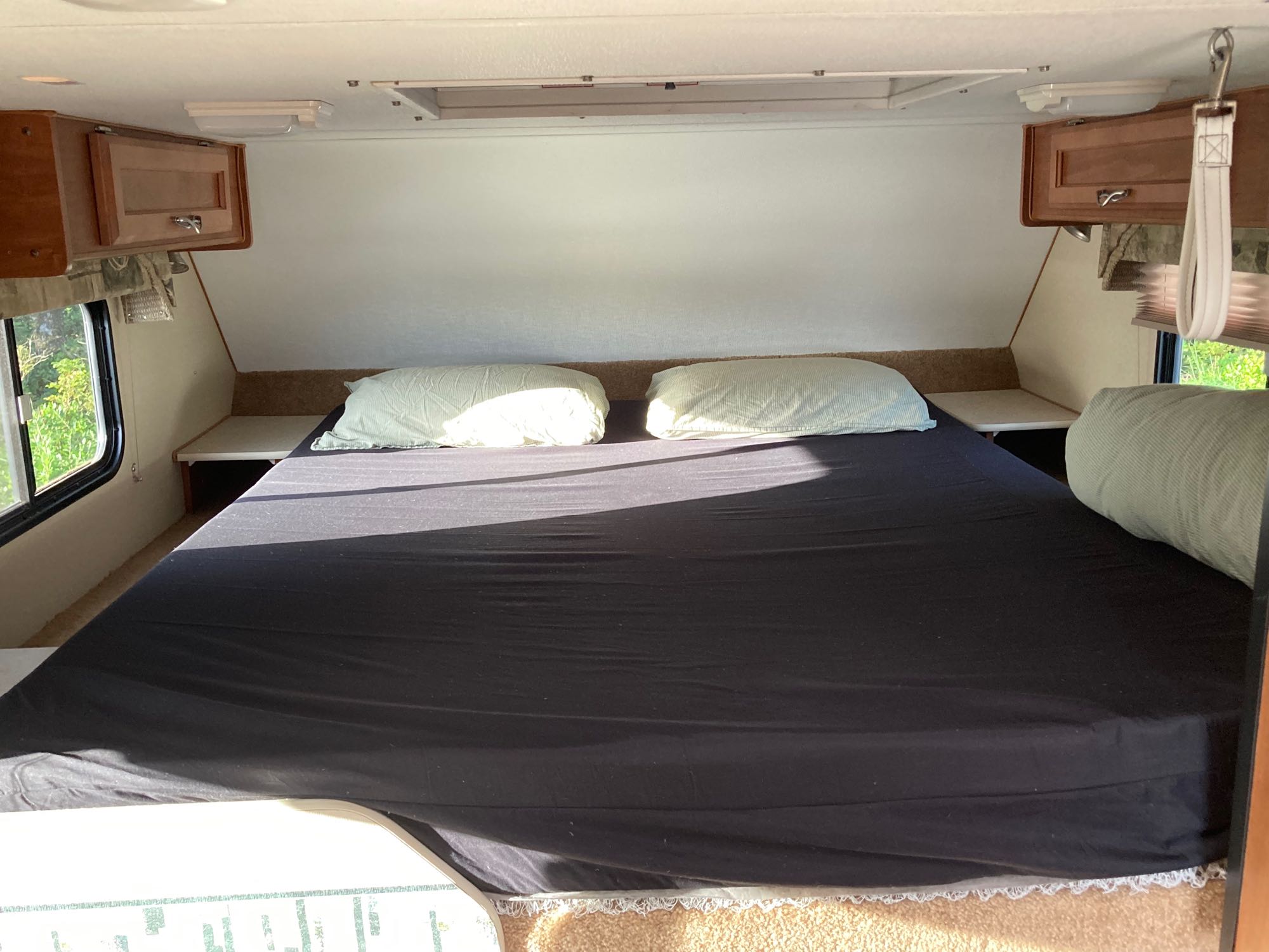 Cozy RV rental bedroom featuring a spacious bed, two pillows, overhead cabinets, and small side shelves.. Dodge RAM 3500HD 2010