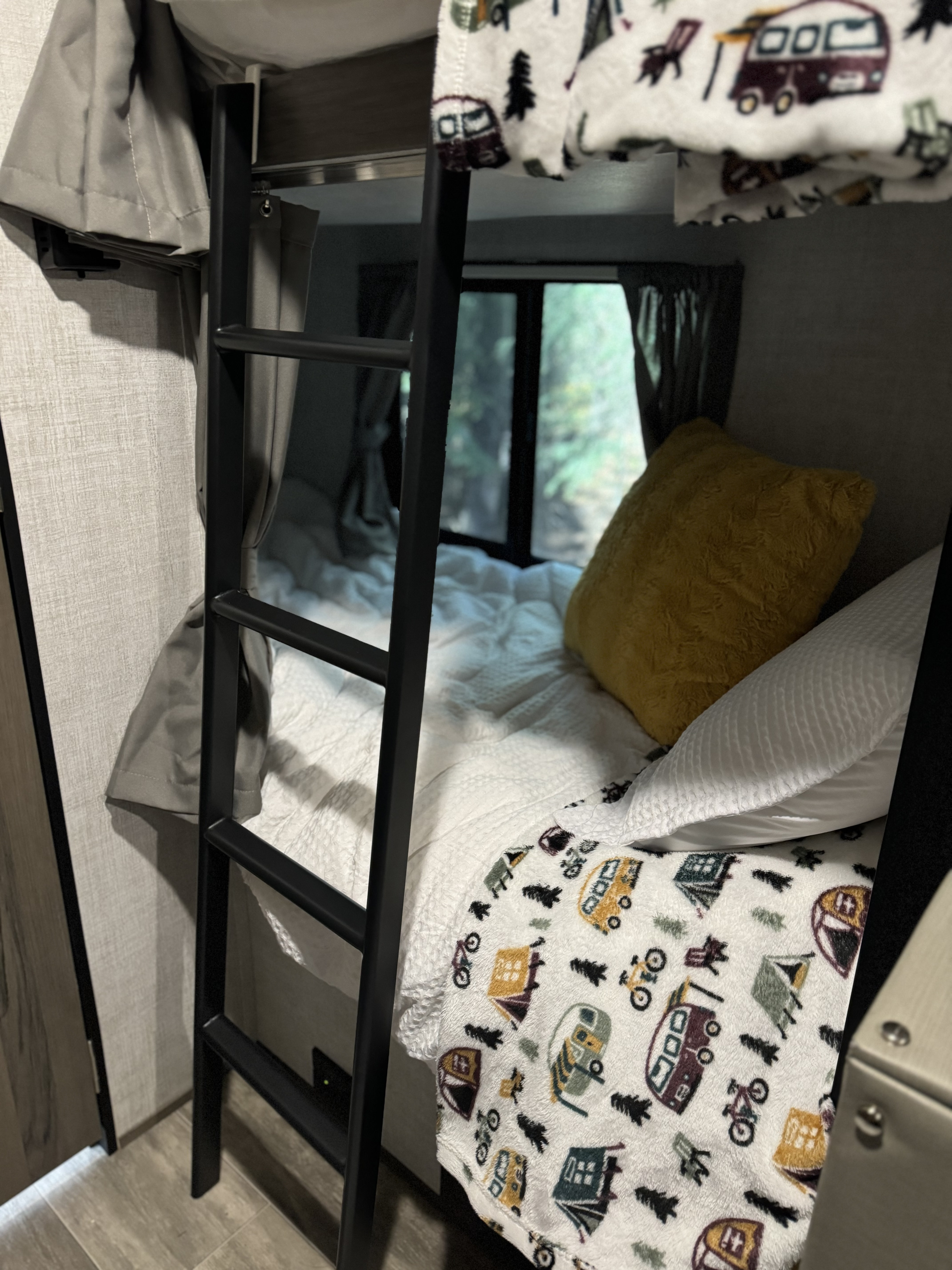 Cozy RV rental bunk beds with a camping-themed blanket, ladder, and window view of nature.. Gulf Stream Northern Express 2021