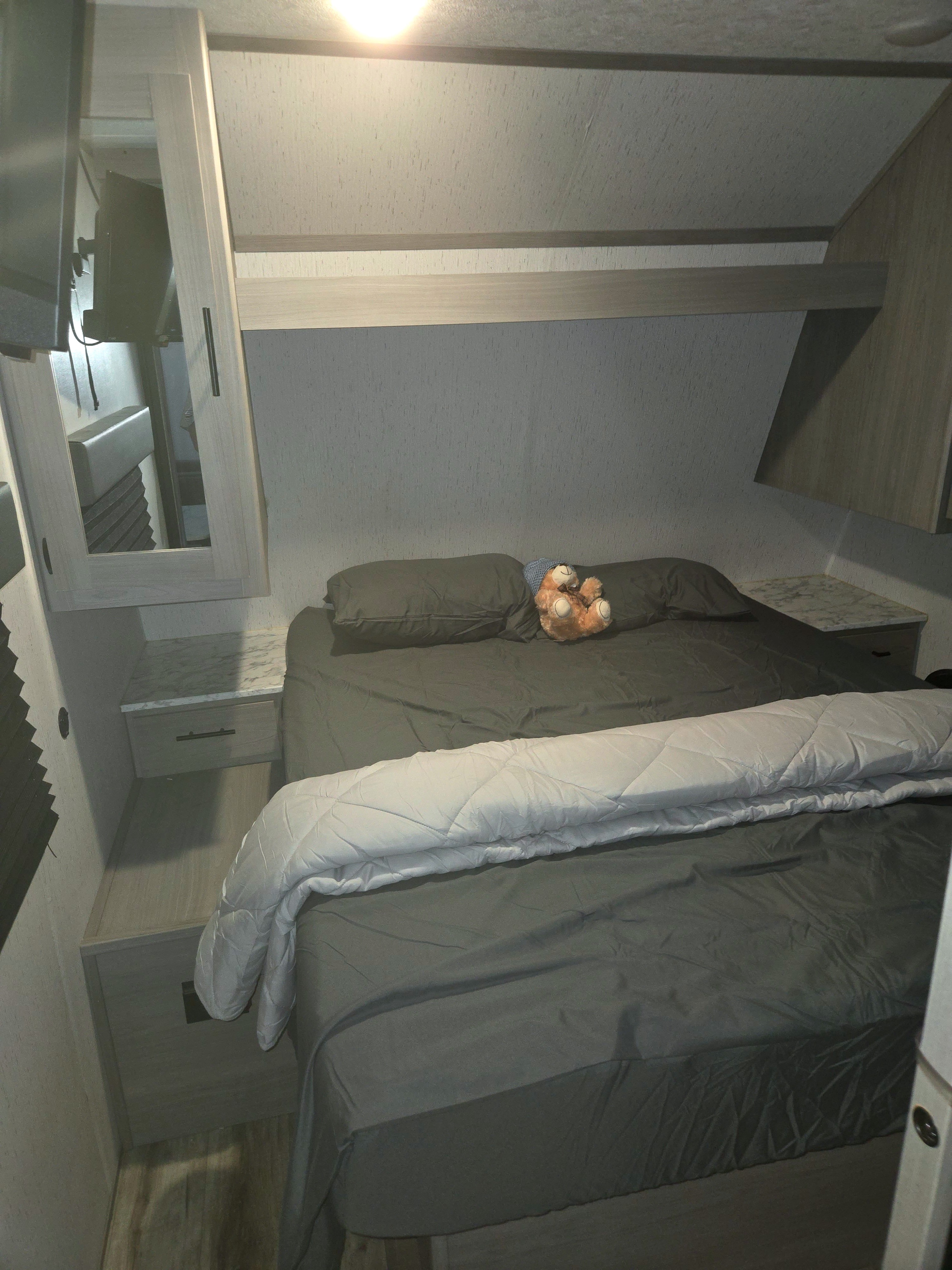 This RV rental bedroom features a comfy bed with dark linens, overhead storage, and side tables, ideal for travel.. Dutchmen Coleman Lantern 2022