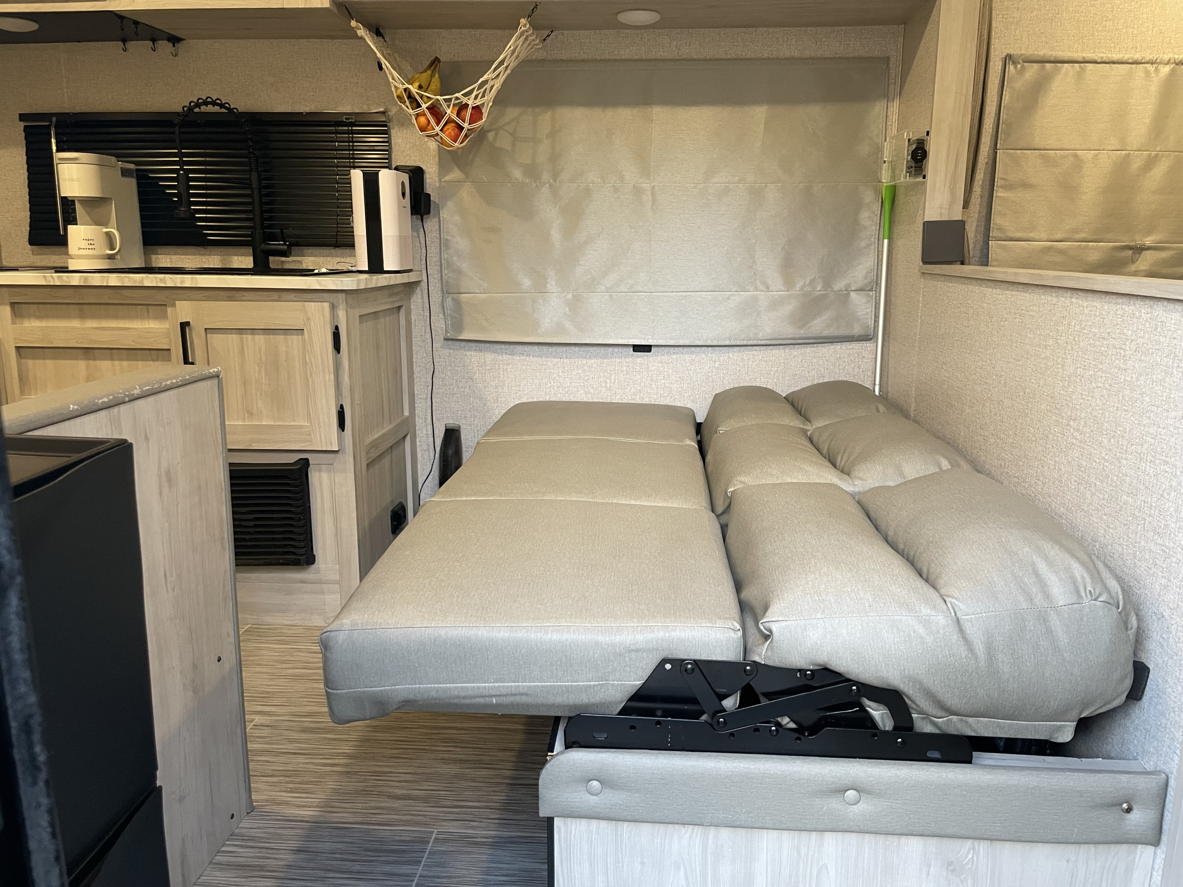 RV rental interior showcasing a compact kitchenette with a coffee maker and a light-colored sofa converting to a bed.. East to West Silver Lake LE 2023