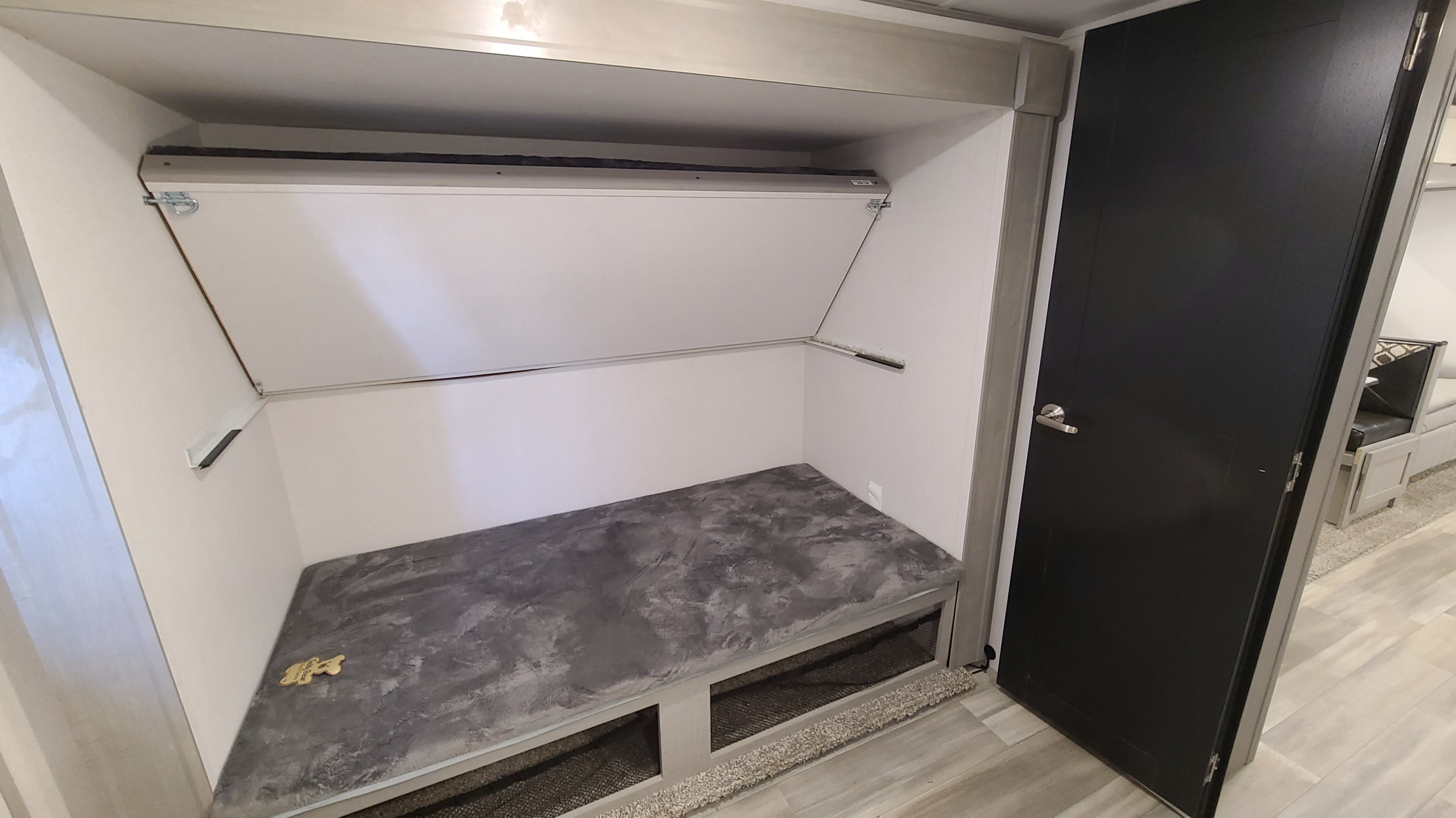 RV rental bunk bed area: a foldable upper bunk, lower bench with under-bed storage, and a dark door.. Forest River Tracer 2021