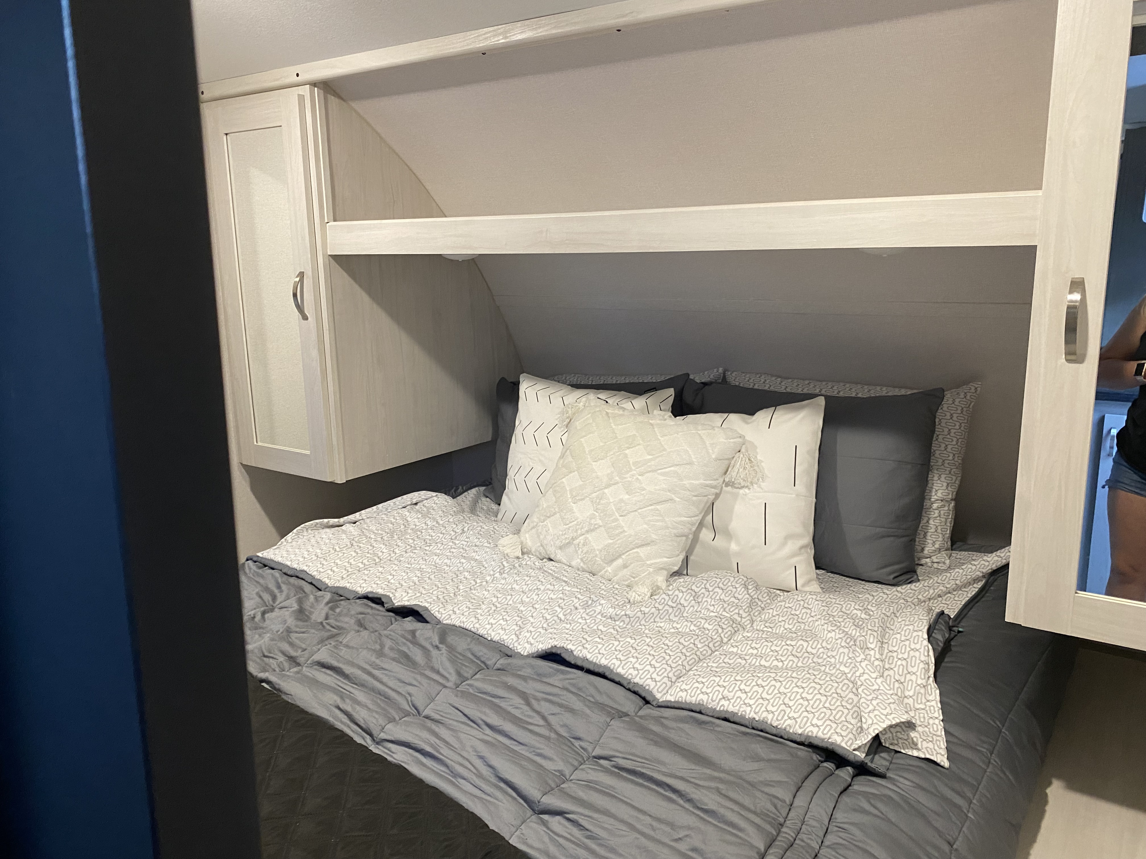 A cozy RV rental bedroom interior features gray & white bedding, multiple pillows, and practical overhead storage.. Forest River Tracer 2021