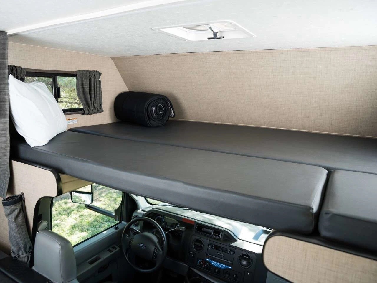 Cozy overhead bunk in an RV rental, featuring a mattress, pillow, and rolled blanket above the driver's cab.. Thor Majestic 2019