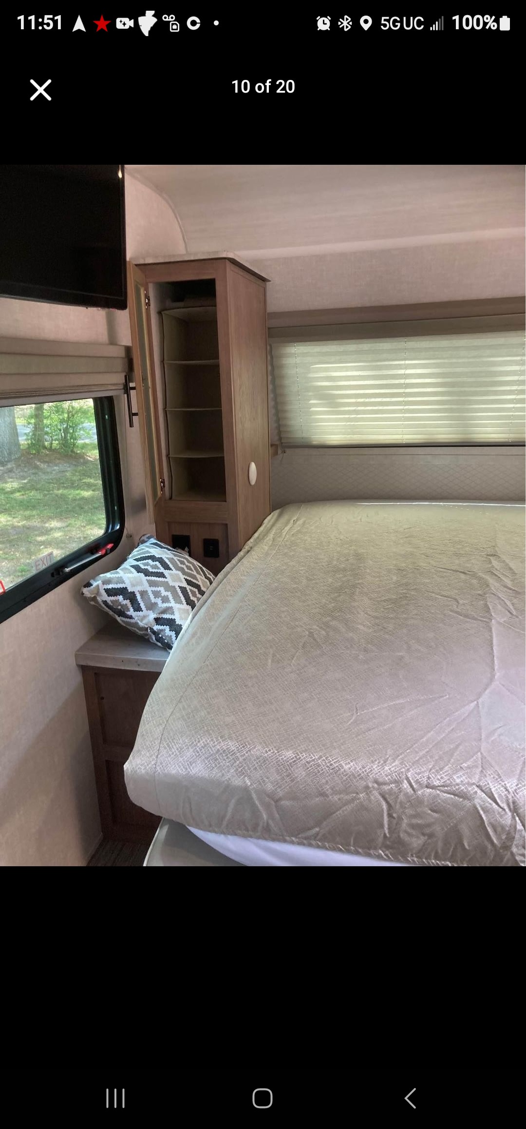 Explore this inviting RV rental bedroom featuring a made bed, window with outdoor view, bedside shelf, and open storage cabinet.. No Boundaries 19 2021