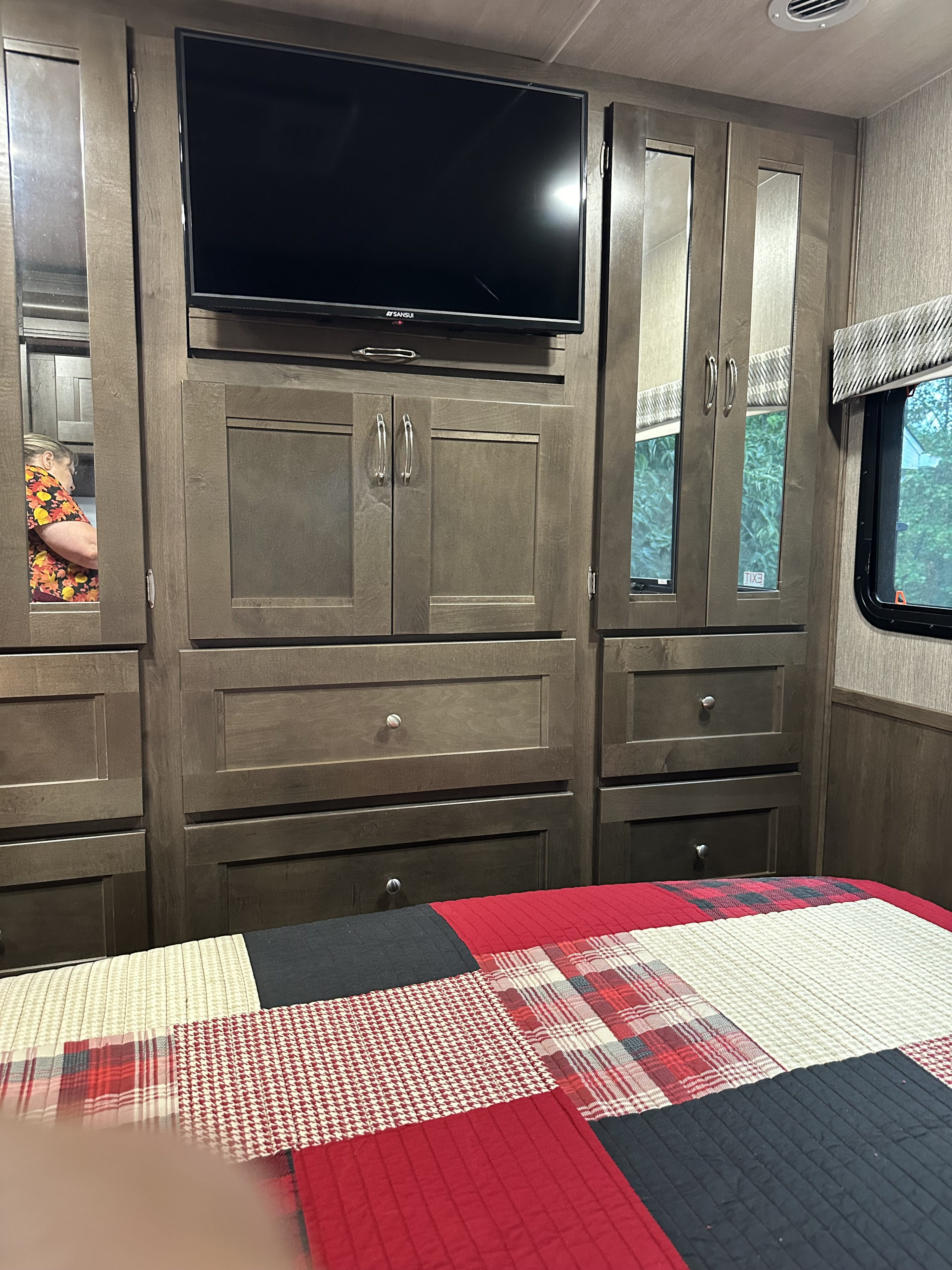 RV rental bedroom: Features built-in wooden storage, TV, mirrored wardrobe, and patterned bedding for a cozy, functional space.. Nexus RV Wraith 2022