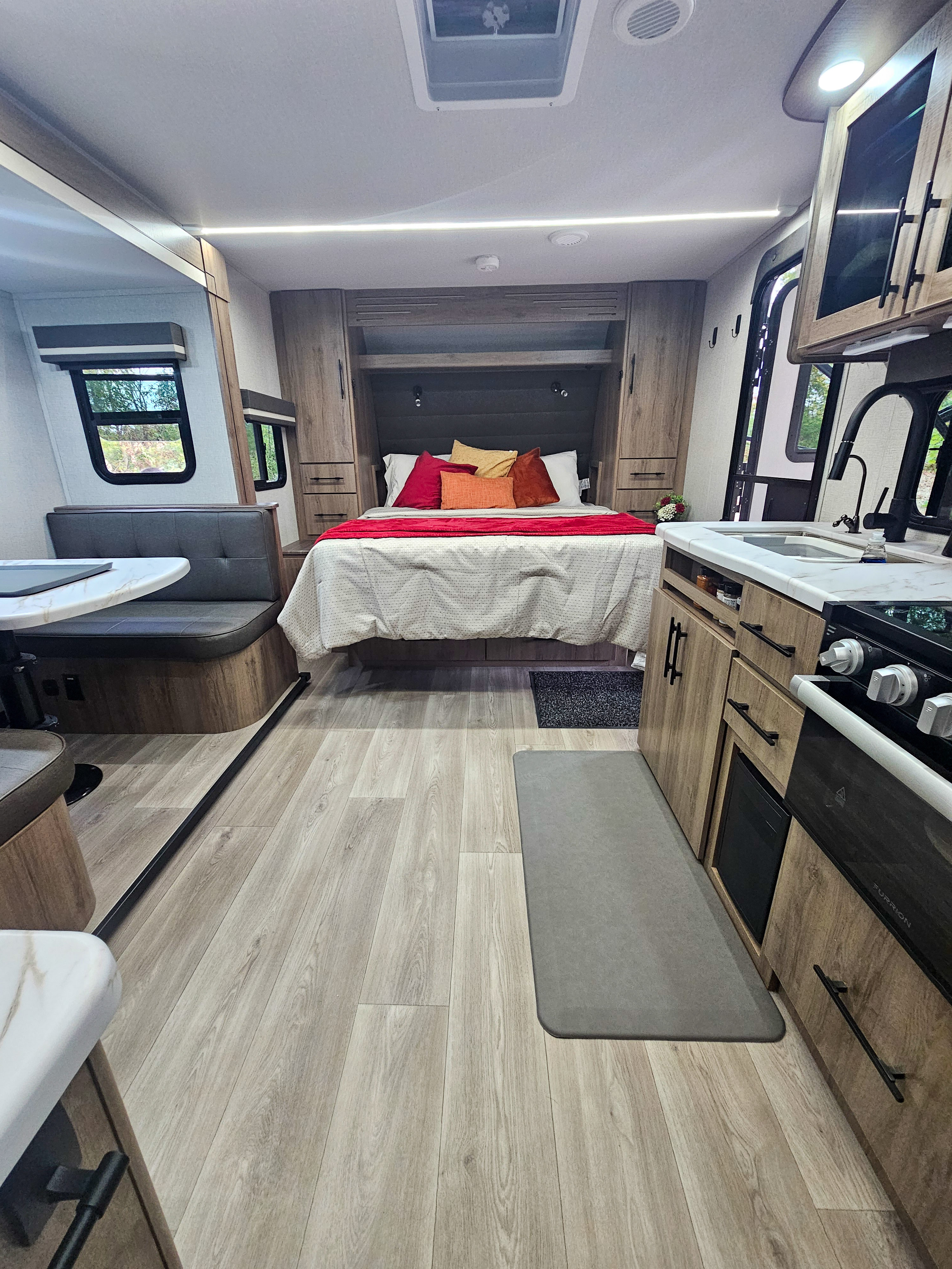 Modern RV rental: a bright interior with light wood flooring, a cozy bed, kitchen, and dining area.. Grand Design Imagine XLS 2024