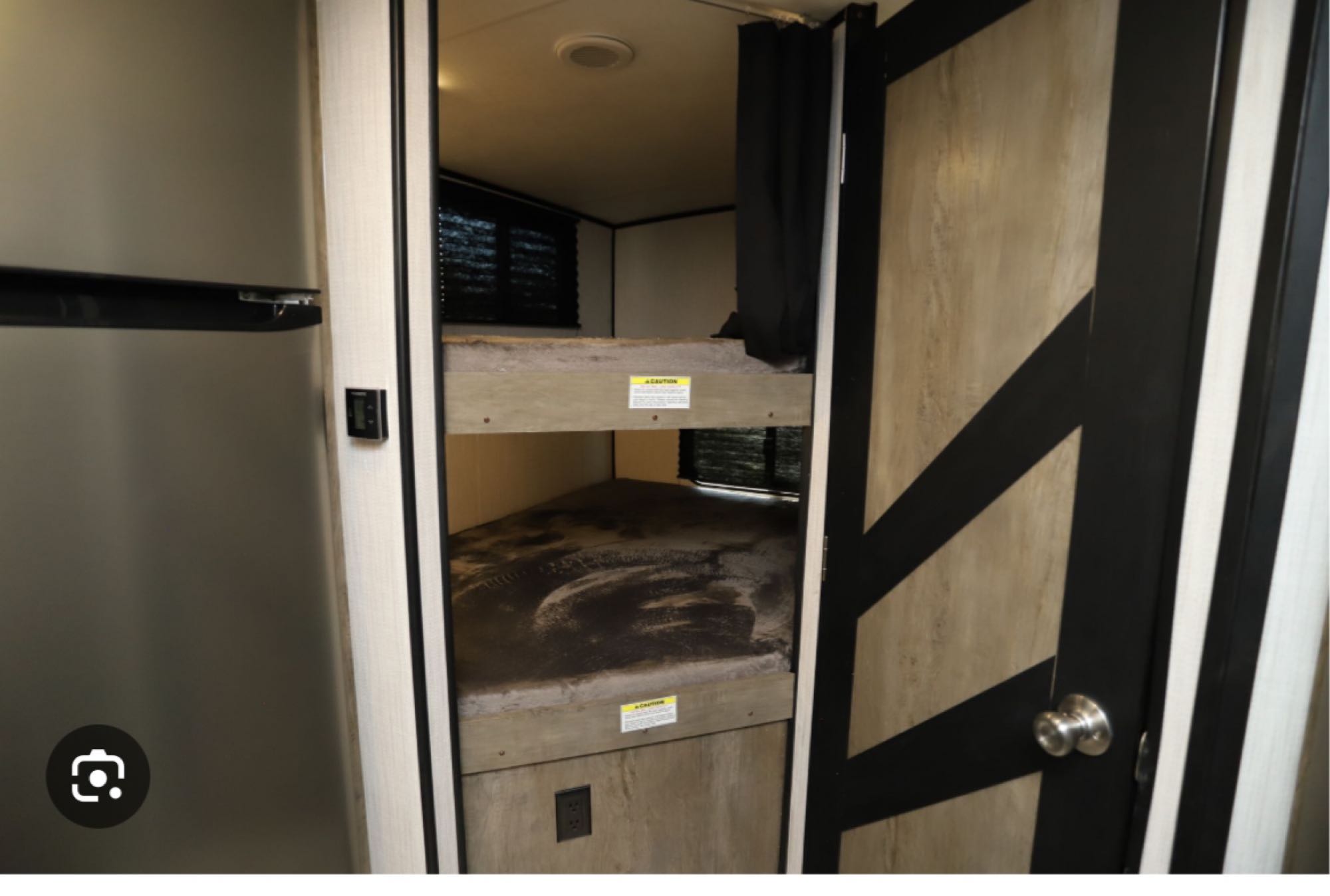 RV rental interior. Left: silver fridge. Center: dusty bunk beds with caution labels. Right: modern patterned door.. Heartland RVs North Trail 2021