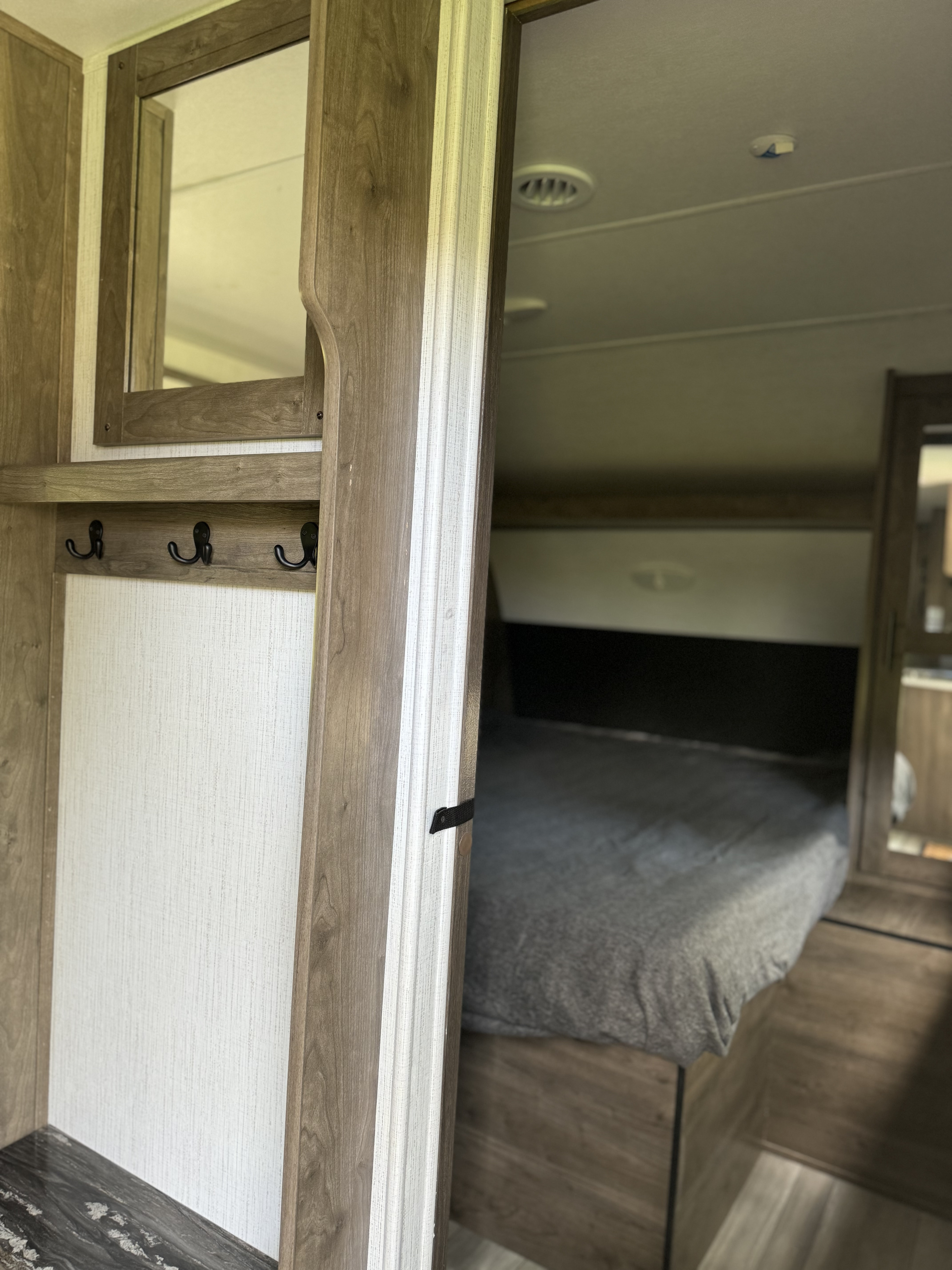 This RV rental interior features a built-in mirror, convenient coat hooks, and a cozy bedroom area with a comfortable bed.. Heartland RVs Pioneer 2023