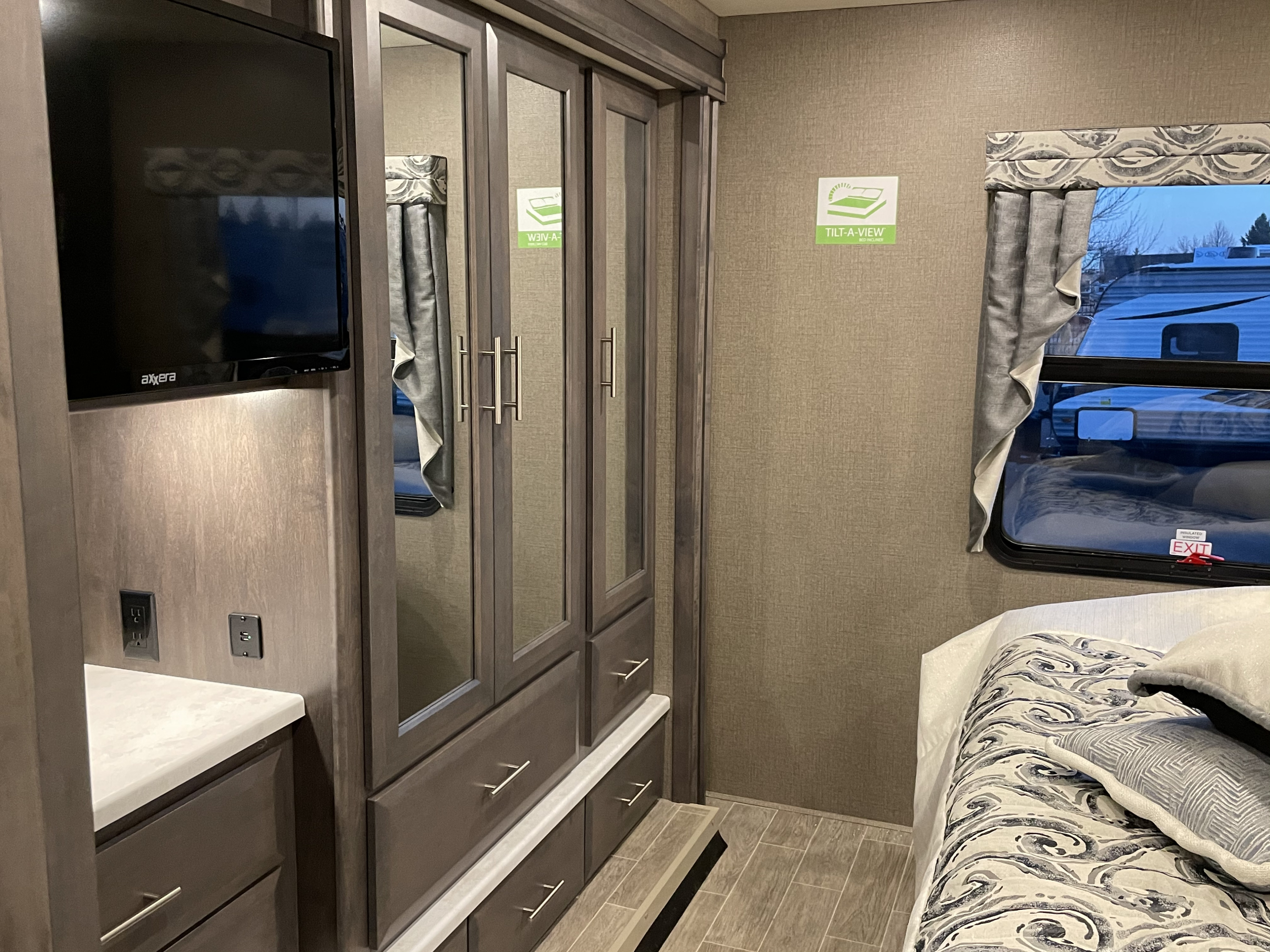 Cozy RV rental bedroom with TV, ample storage, and a TILT-A-VIEW bed, offering comforts for your journey.. Thor Miramar 2021