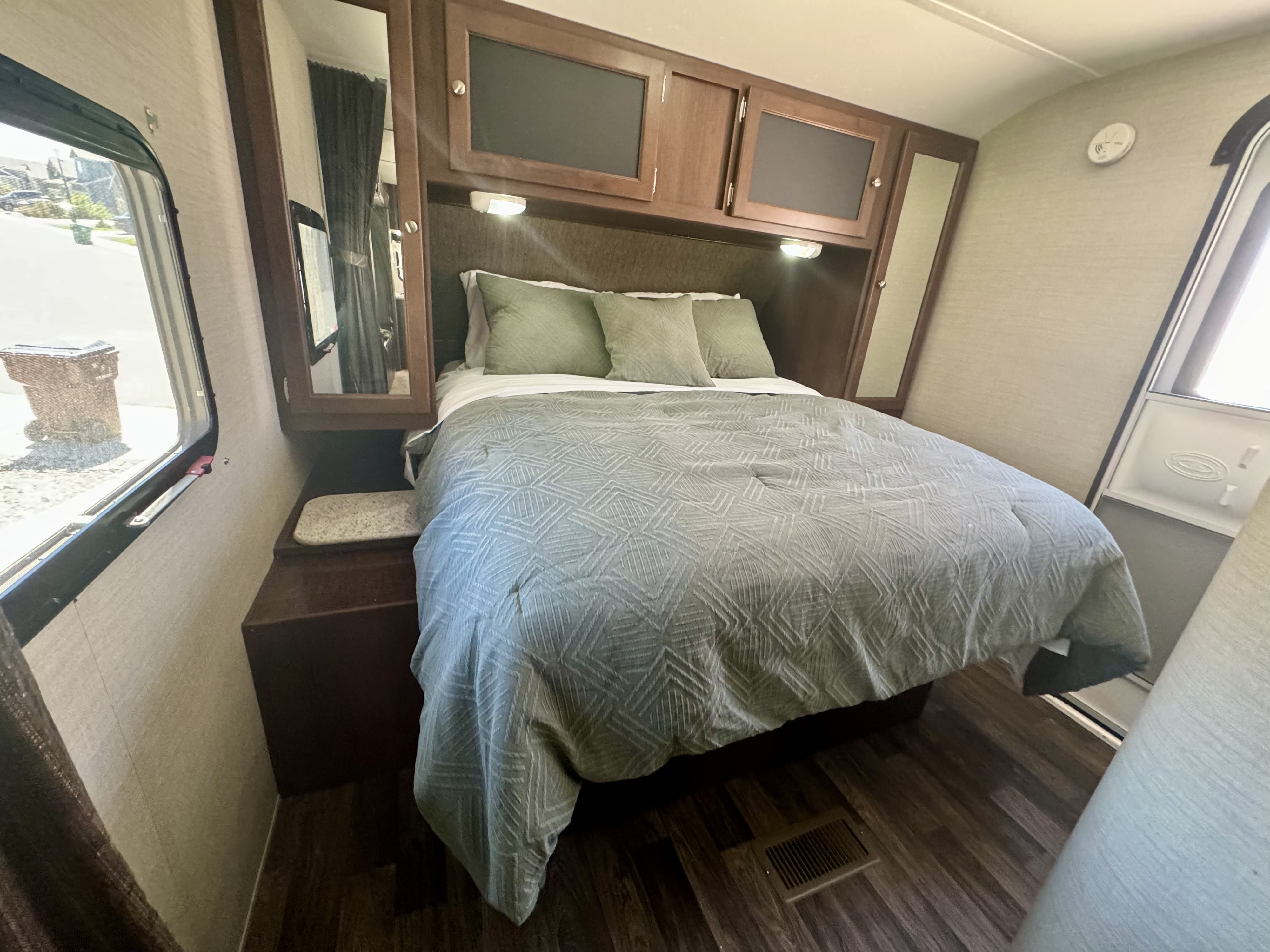Interior view of a comfortable RV rental bedroom, featuring a bed, wooden overhead cabinets, and a large window.. Keystone RV Bullet Ultra Lite 2015