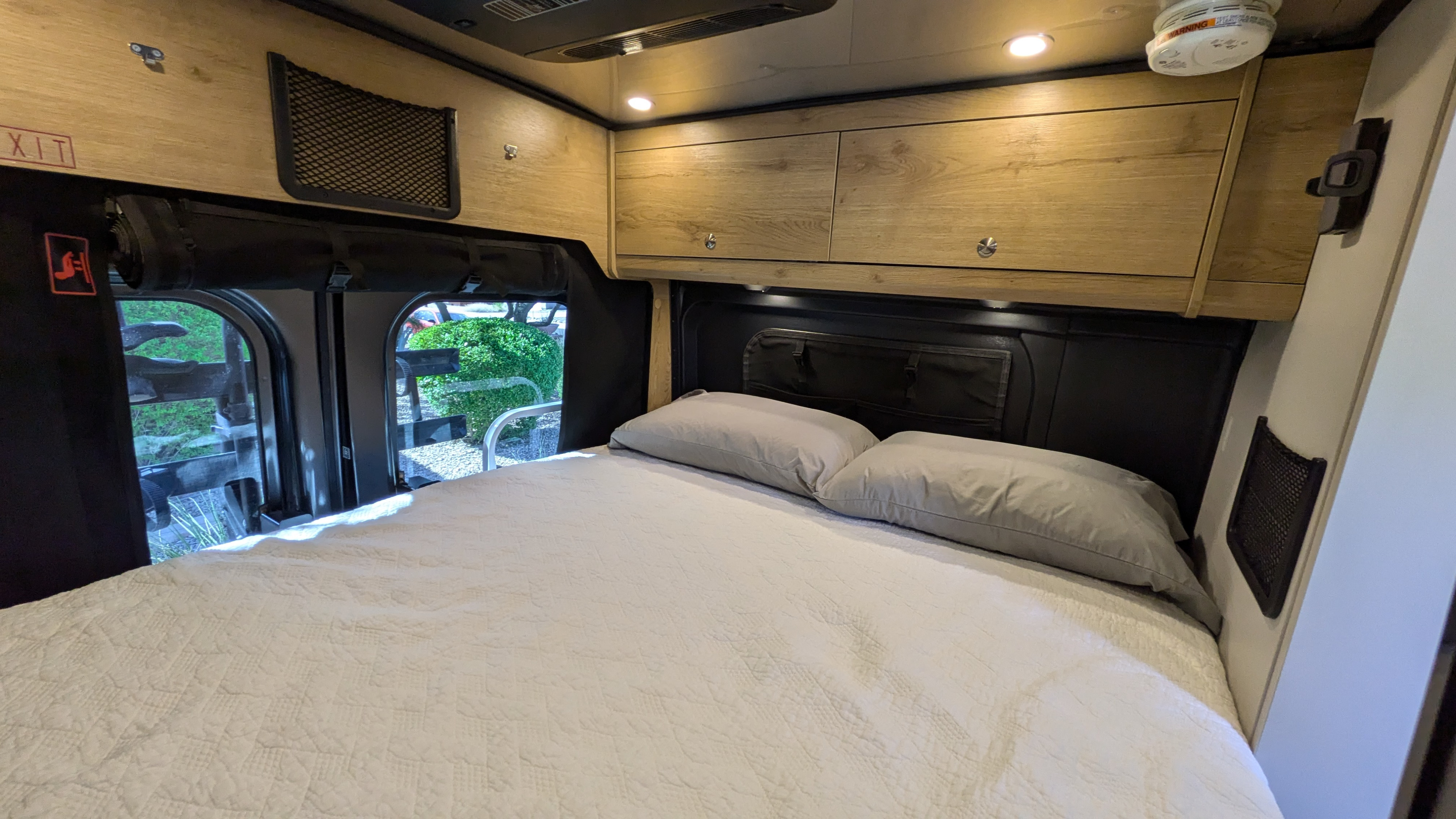 Inside an RV rental, a compact bedroom with a comfy bed, overhead storage, ambient lighting, and views.. Airstream Rangeline 2023