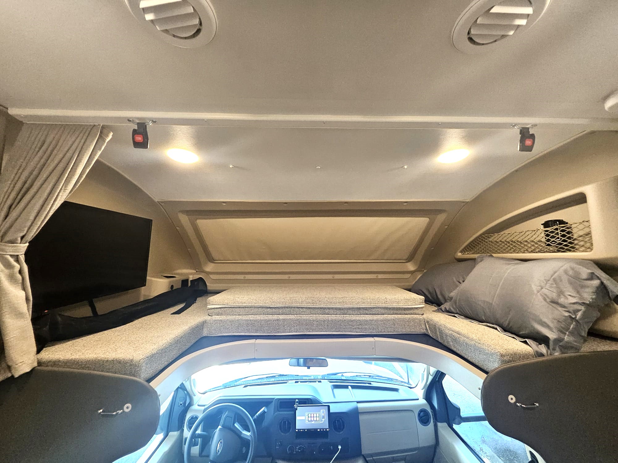 Spacious cab-over bunk with a TV above the driver's cabin in an RV rental, offering comfortable sleeping.. Jayco Redhawk 2024