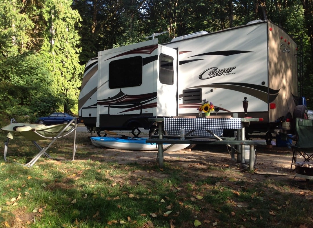 Spacious RV rental set up for camping, complete with picnic table, kayaks, and hammock in a wooded site.. Keystone RV Cougar 2015