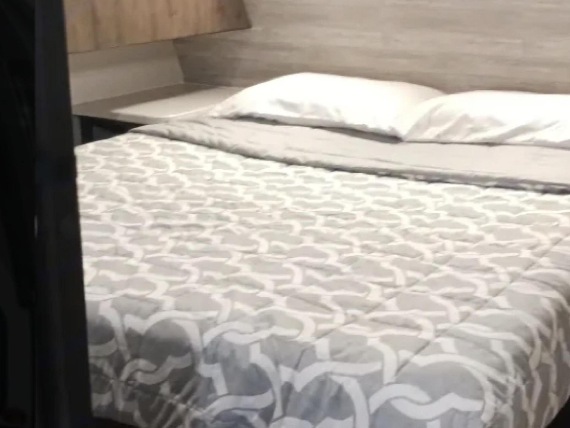 This RV rental bedroom features a cozy bed with white pillows and a grey patterned comforter, ideal for travelers.. Heartland RVs Mallard 2020