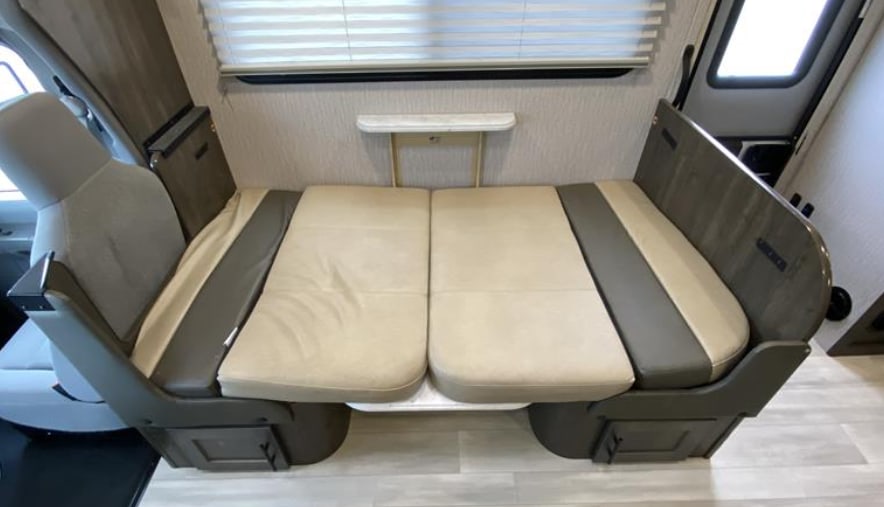 Explore this RV rental's cozy dinette area. Features opposing cushioned benches & a wall-mounted shelf, perfect for meals on the road.. Forest River Coachmen Leprechaun 2023