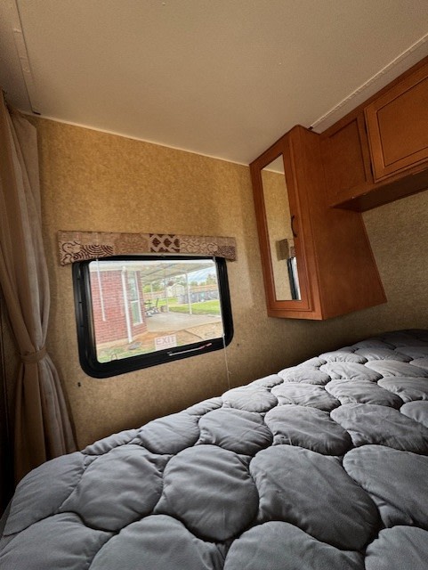 RV rental bedroom with quilted grey comforter, window, and overhead storage for a comfortable stay.. Gulf Stream Kingsport SE 2014
