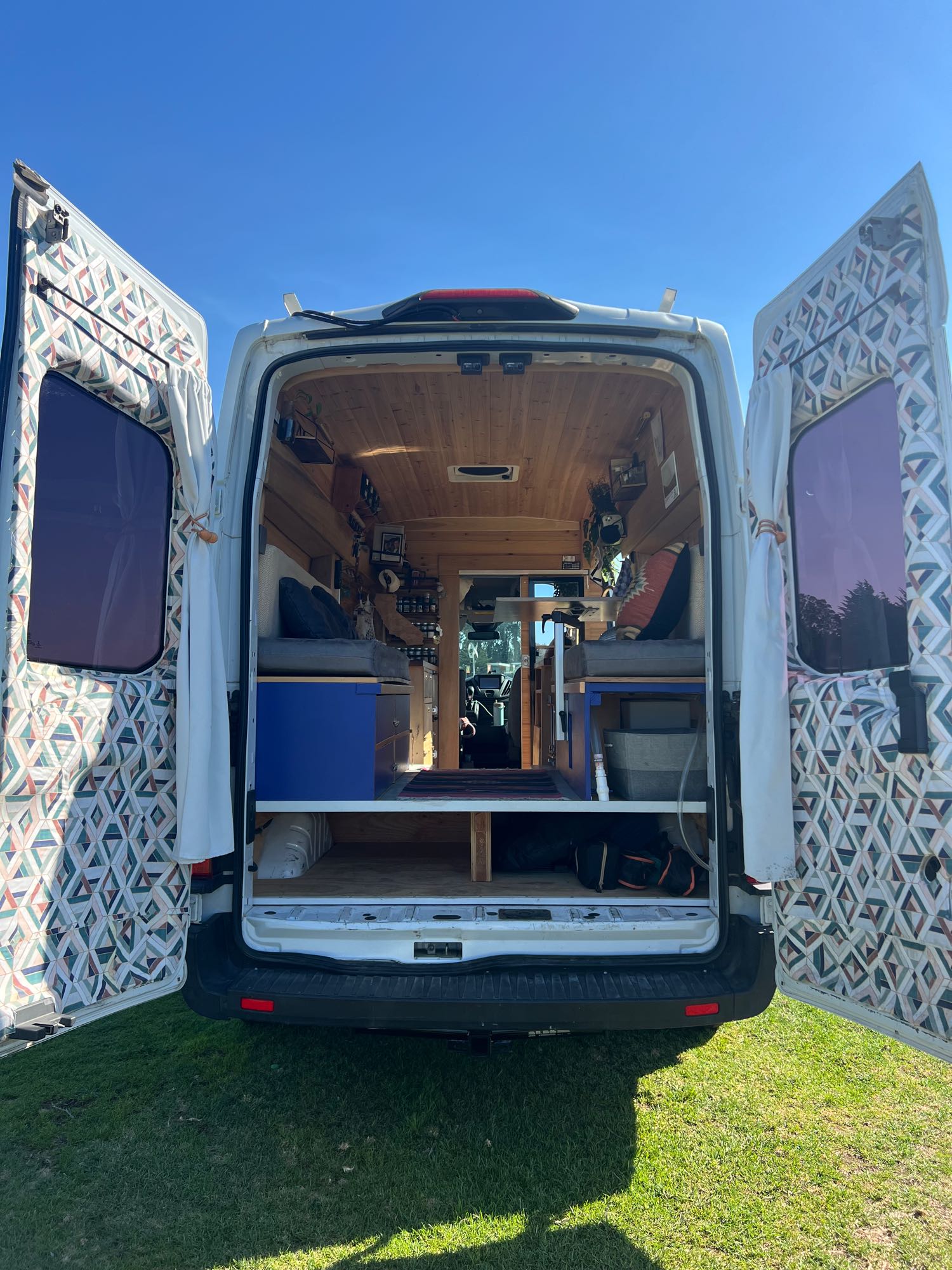 Inside an RV rental: a custom camper van conversion, featuring wood ceilings, comfy beds, & vibrant patterned doors.. Ford Transit 2019