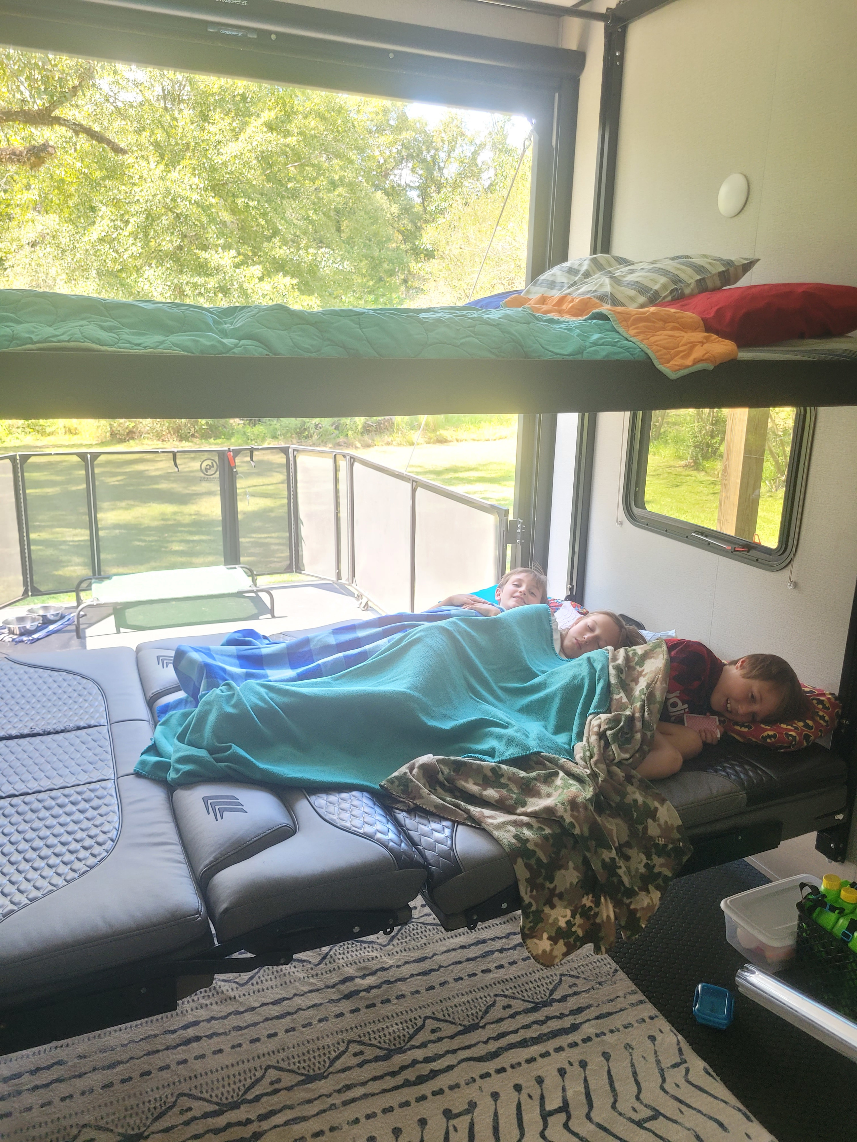 Three kids resting on RV rental bunk beds, enjoying a peaceful family camping trip inside their cozy camper.. Grand Design Momentum 2020