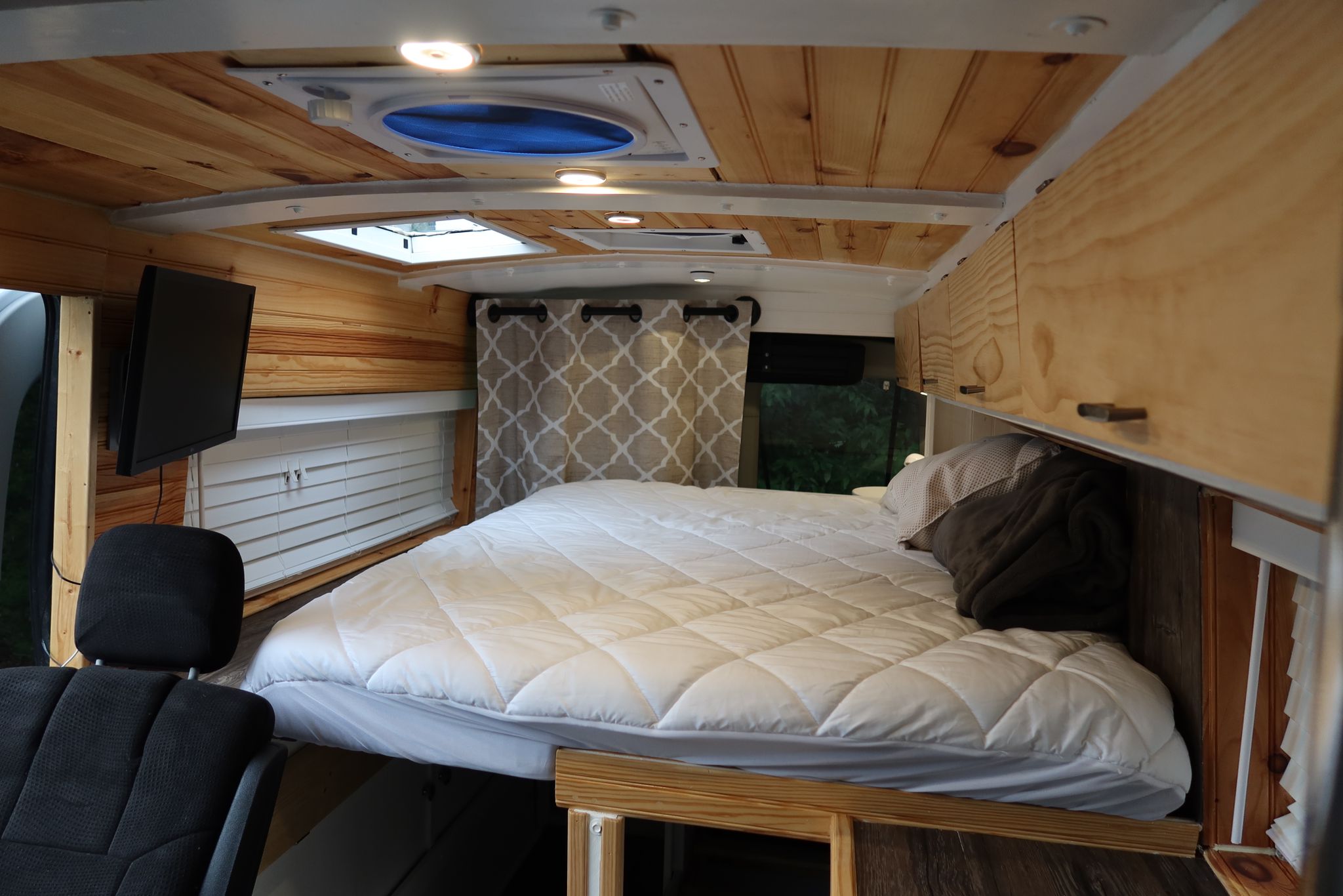 An inviting RV rental interior showcases a cozy bed, wood-paneled walls, TV, and convenient storage, ideal for road trips.. Ford Transit 2017