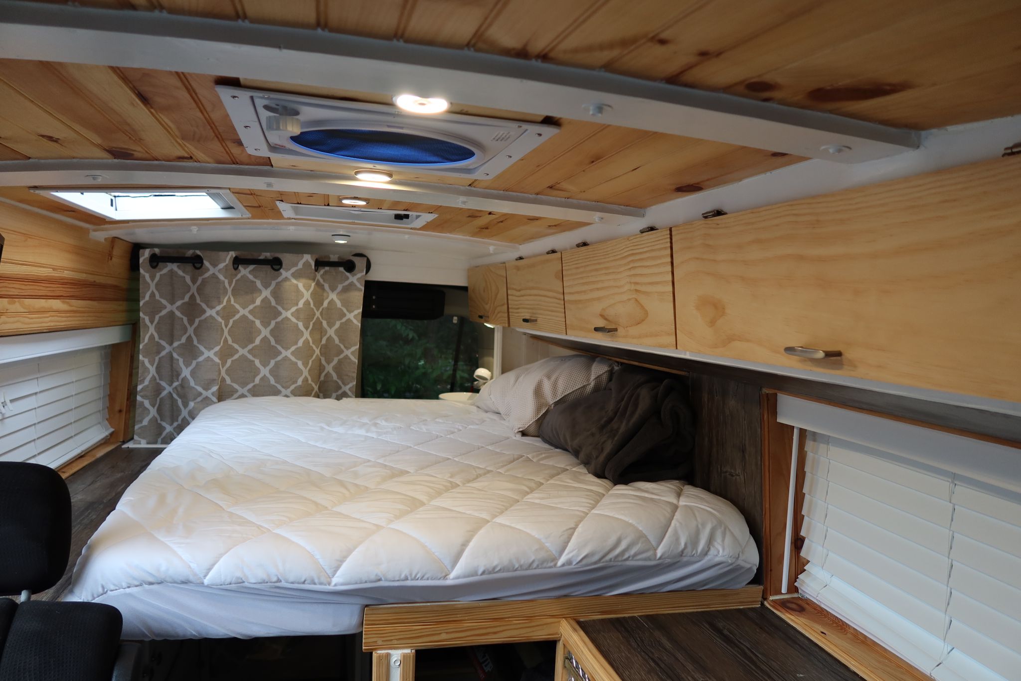 RV rental: Inside a cozy campervan, a bed with white comforter, wooden walls, ceiling fan, and overhead cabinets.. Ford Transit 2017