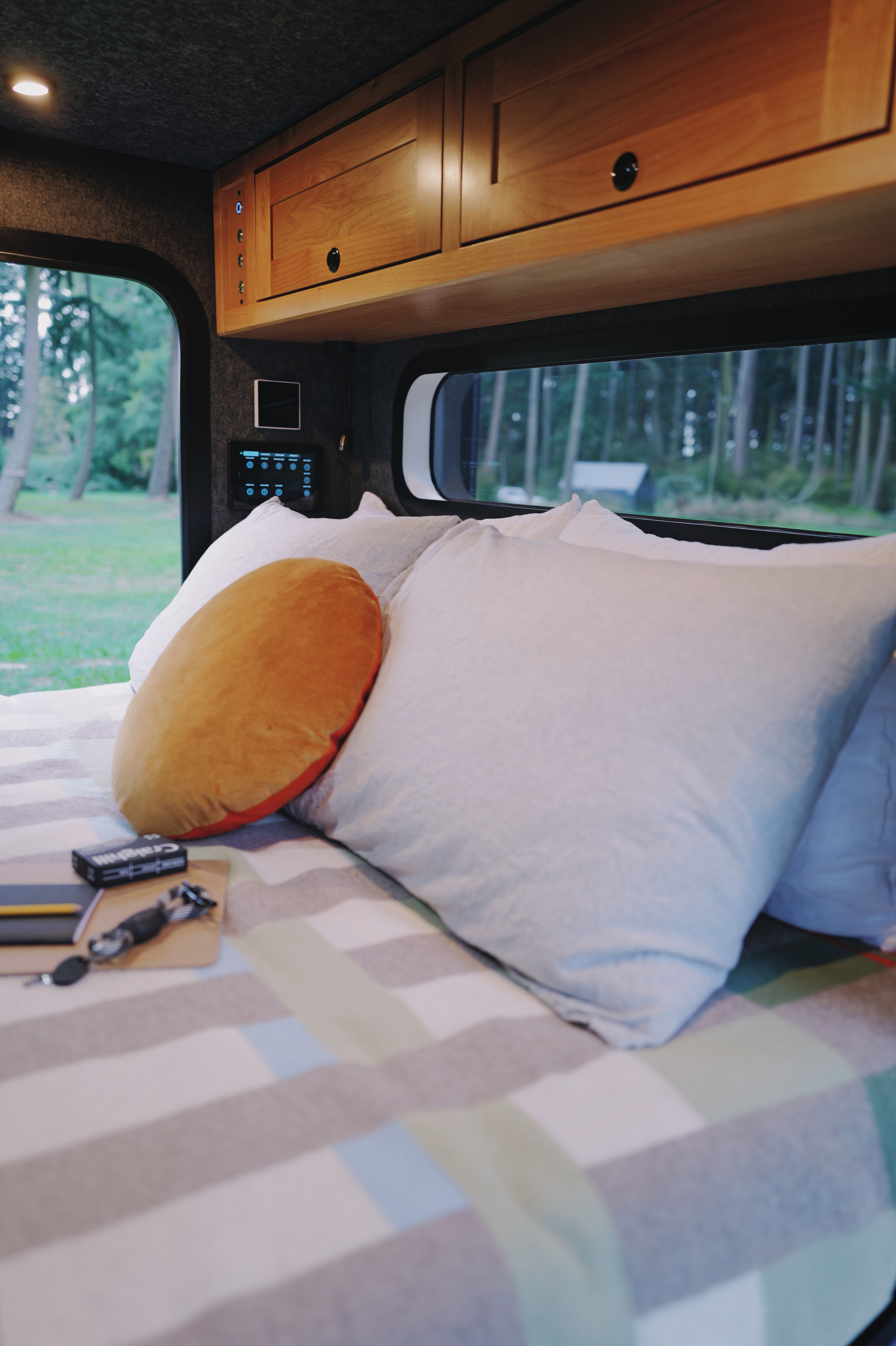 Comfortable rv rental bedroom with soft pillows, striped blanket, smart controls, wooden cabinets, and a serene forest view.. Campworks NS-1 Electrified Pro 2024